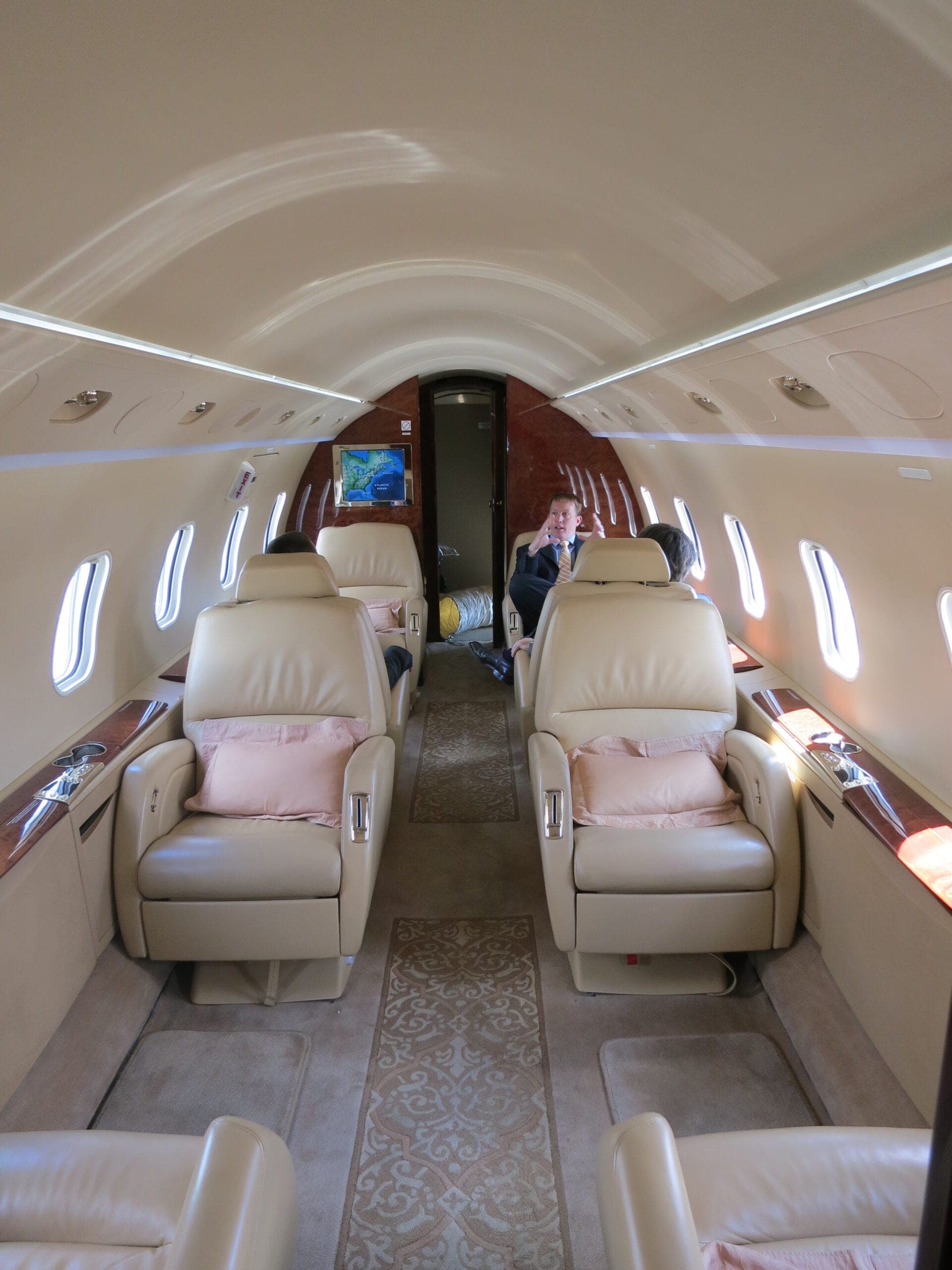 Bombardier Challenger 300 Interior from front of cabin looking towards the back. White leather seats with pink cushions and man in background