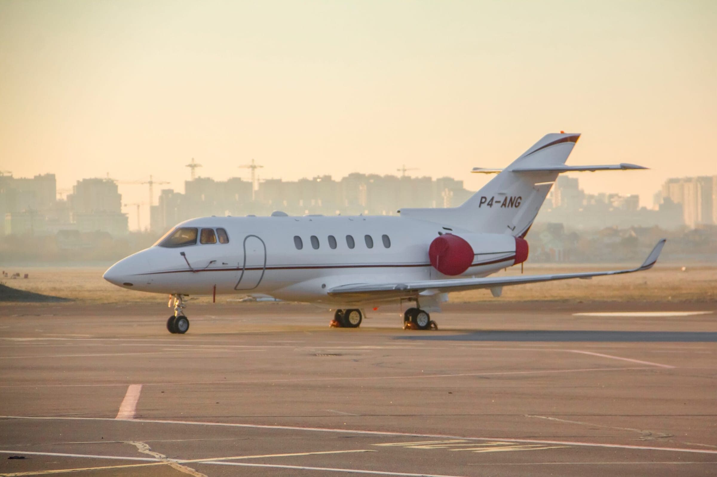 Hawker 900XP private jet reg number P4-ANG with engine covers on apron at airport at dawn