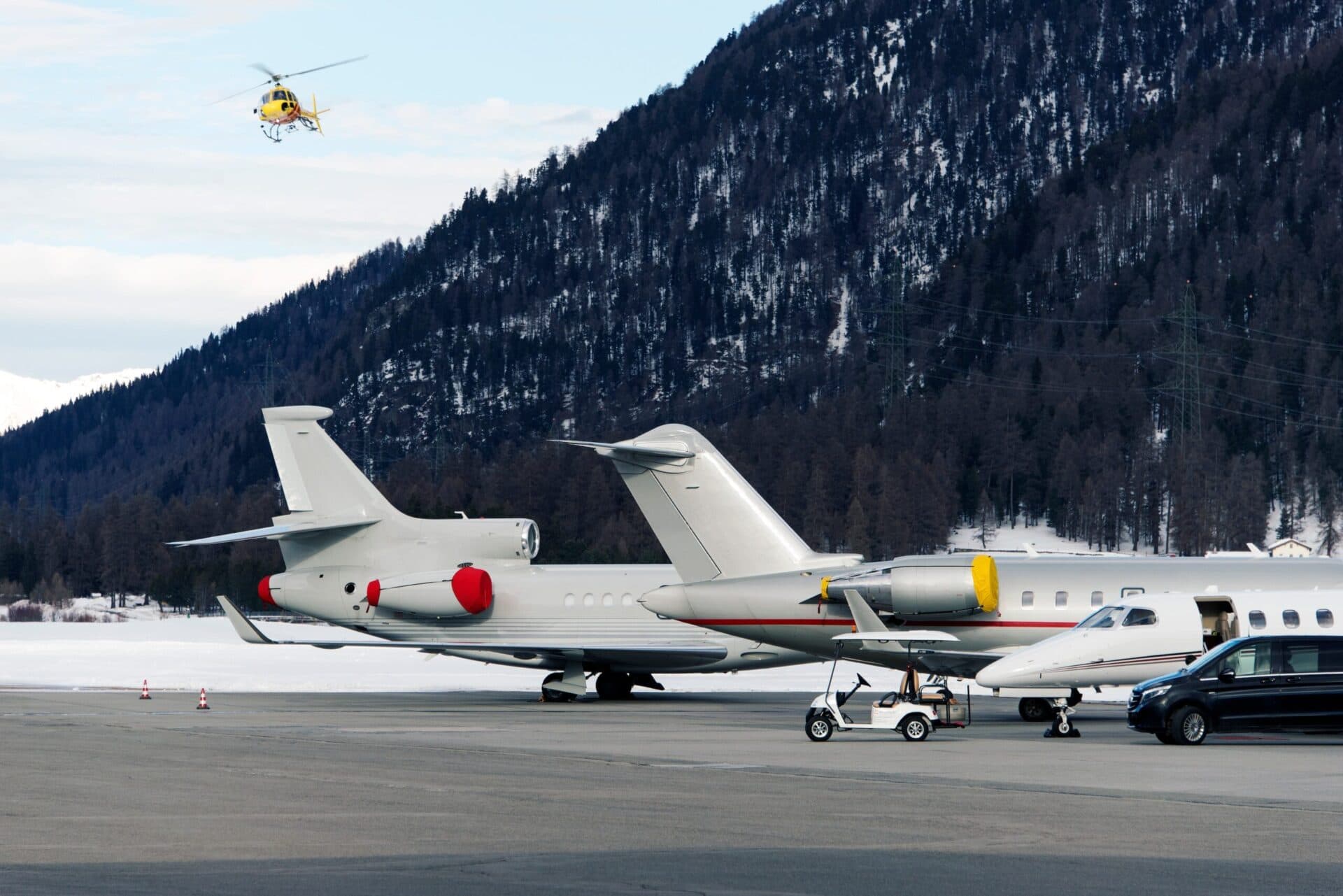 tail of large private jets at snowy airport with helicopter flying overhead