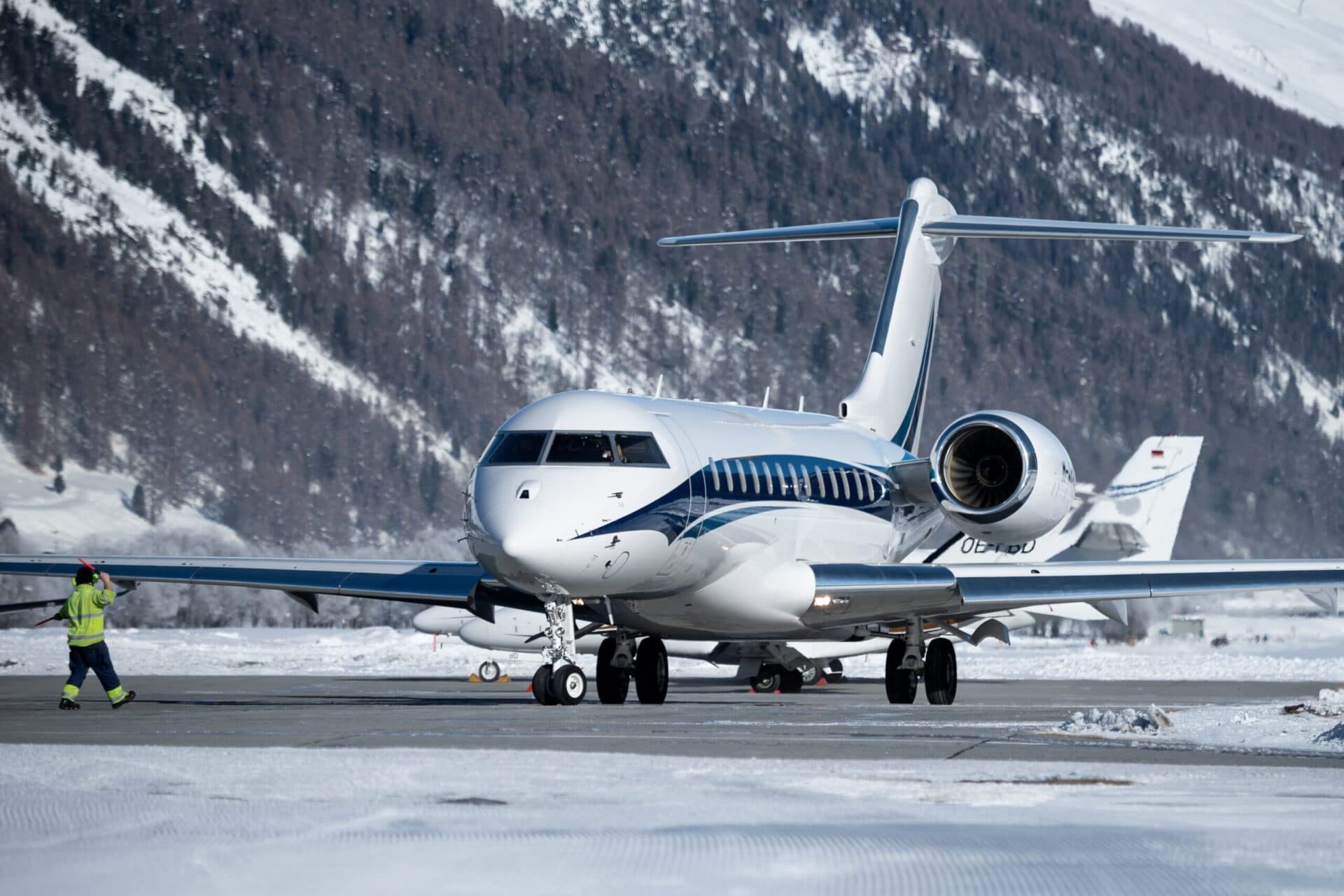 Bombardier Global 7500 taxiing at snowy airport with ground crew in front of it directing