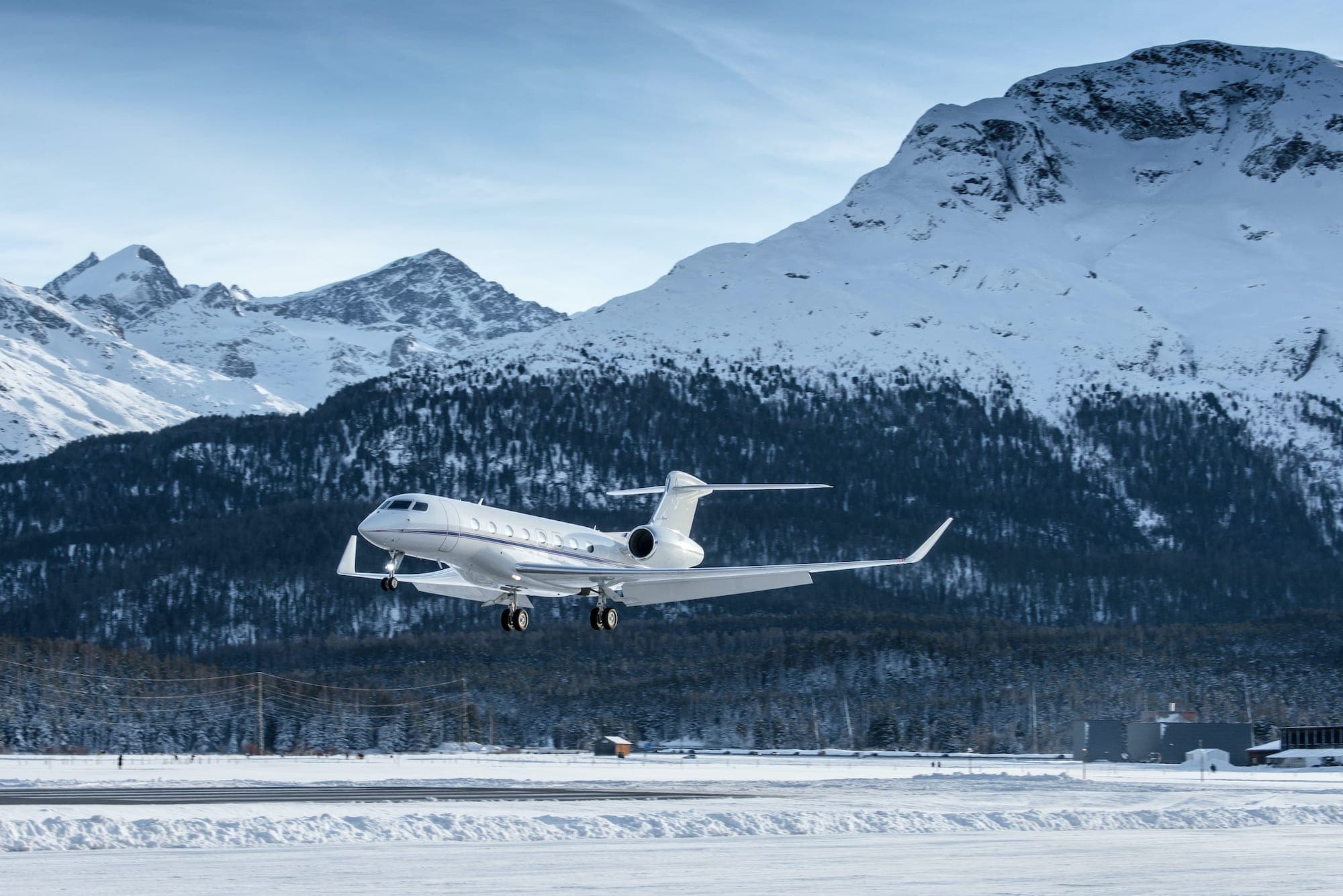 A private jet landing on a snow-lined runway with mountains behind