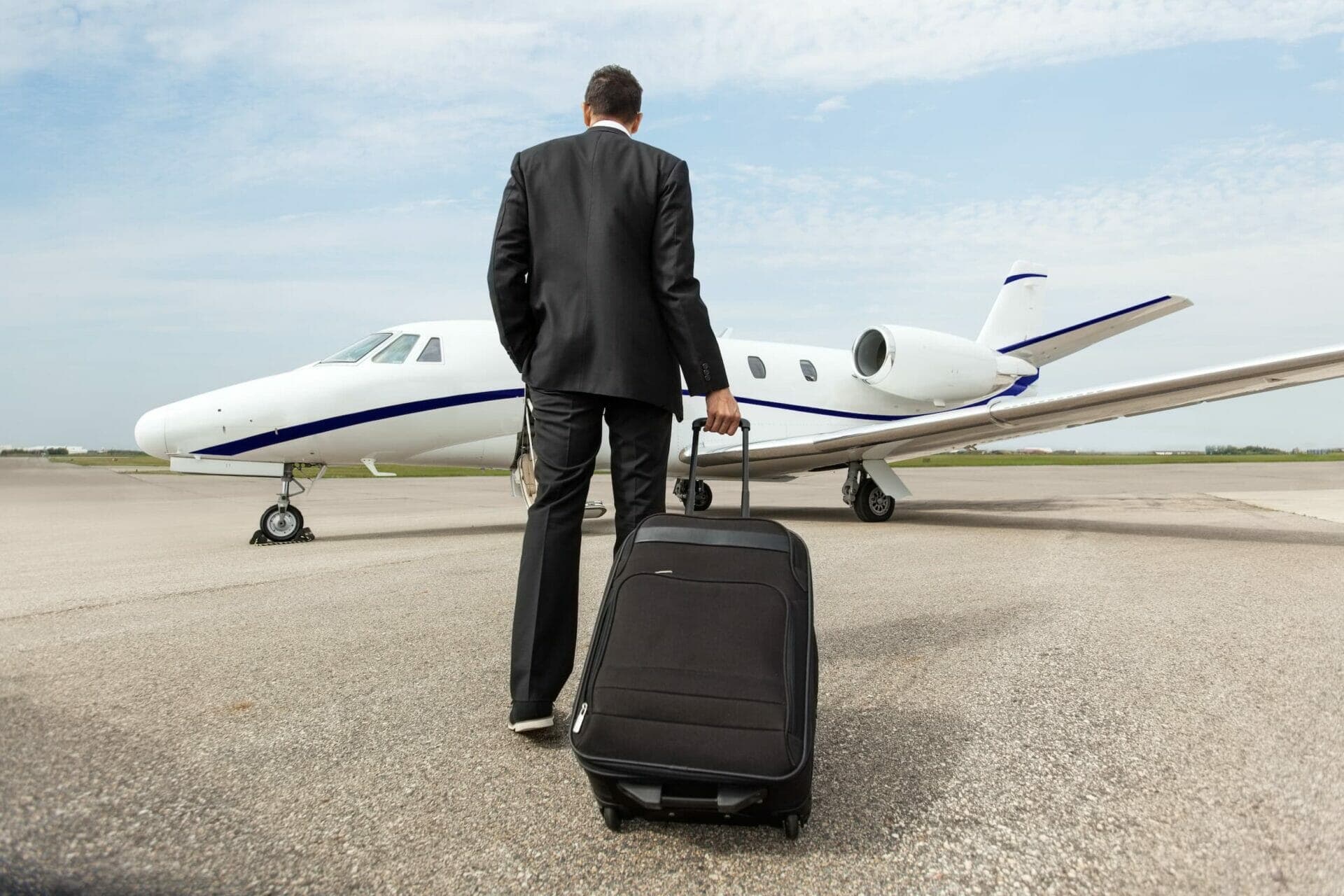 A traveller in a suit wheeling a suitcase toward a waiting private jet