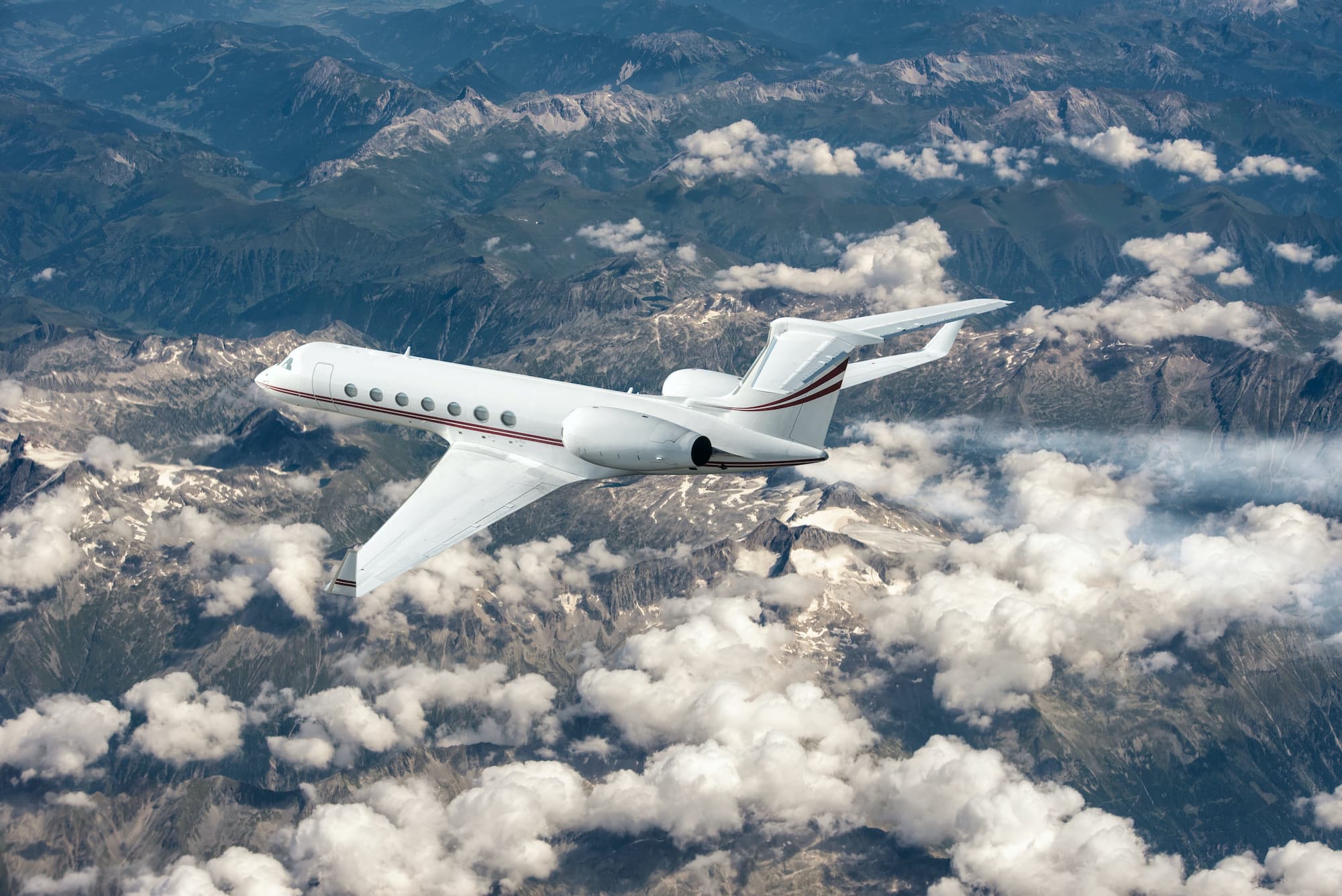 A private jet in flight above the clouds with mountains below