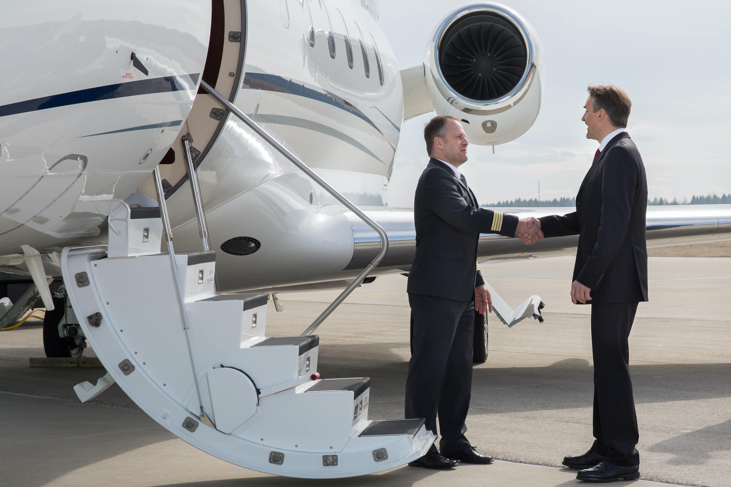 A pilot and a passenger shaking hands at the airstair of a private jet