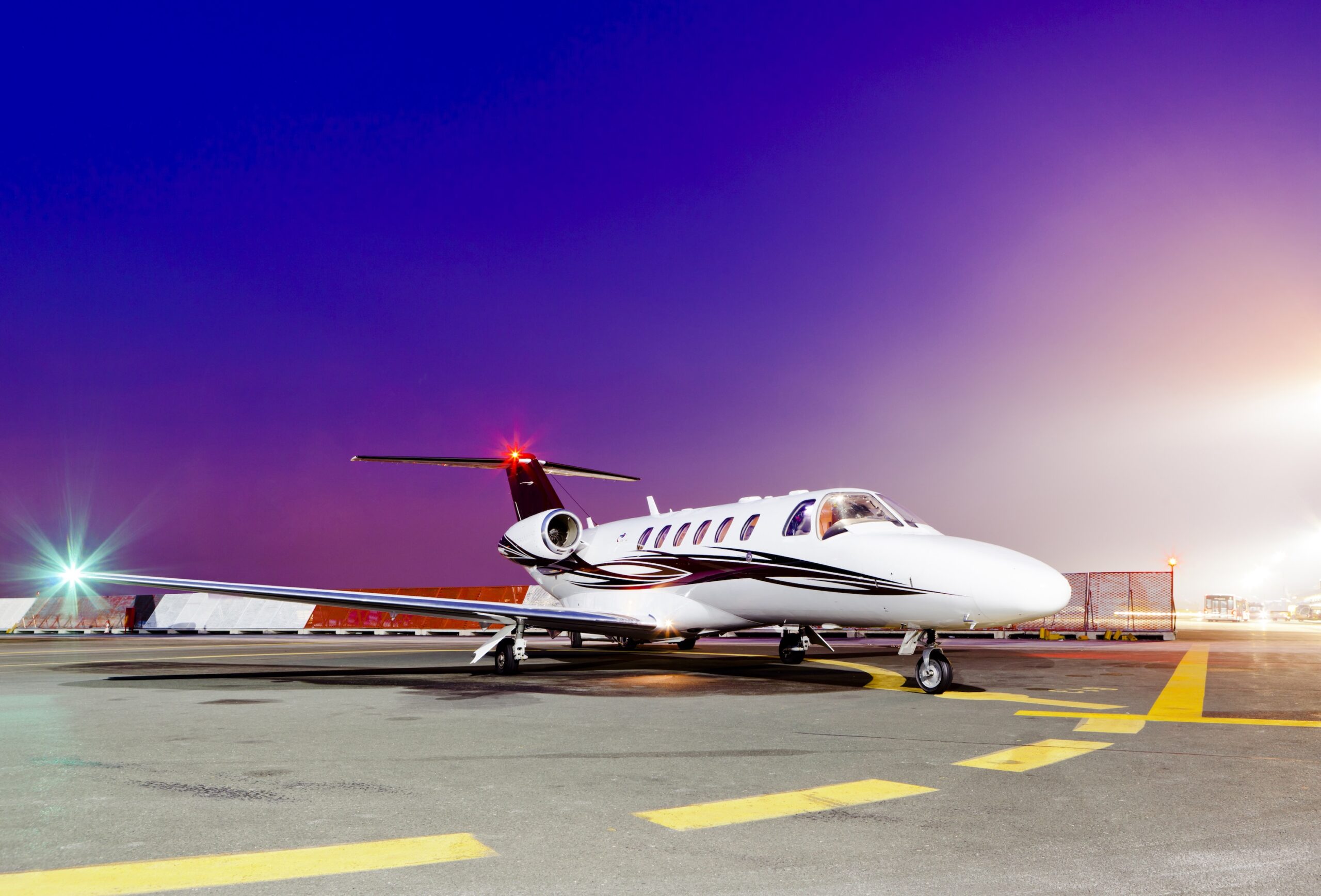 Cessna Citation private jet on apron of airport with navigation lights on with purple sky