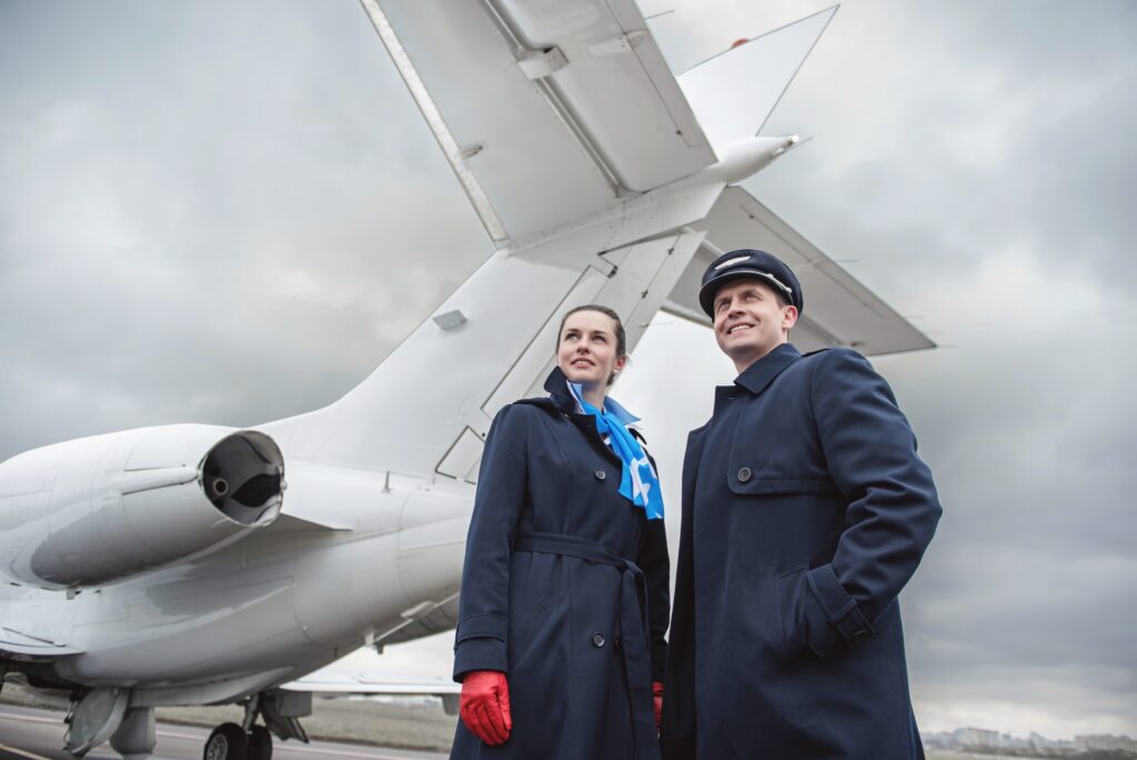Low angle portrait of cheerful air-hostess and glad pilot locating near airplane outdoor