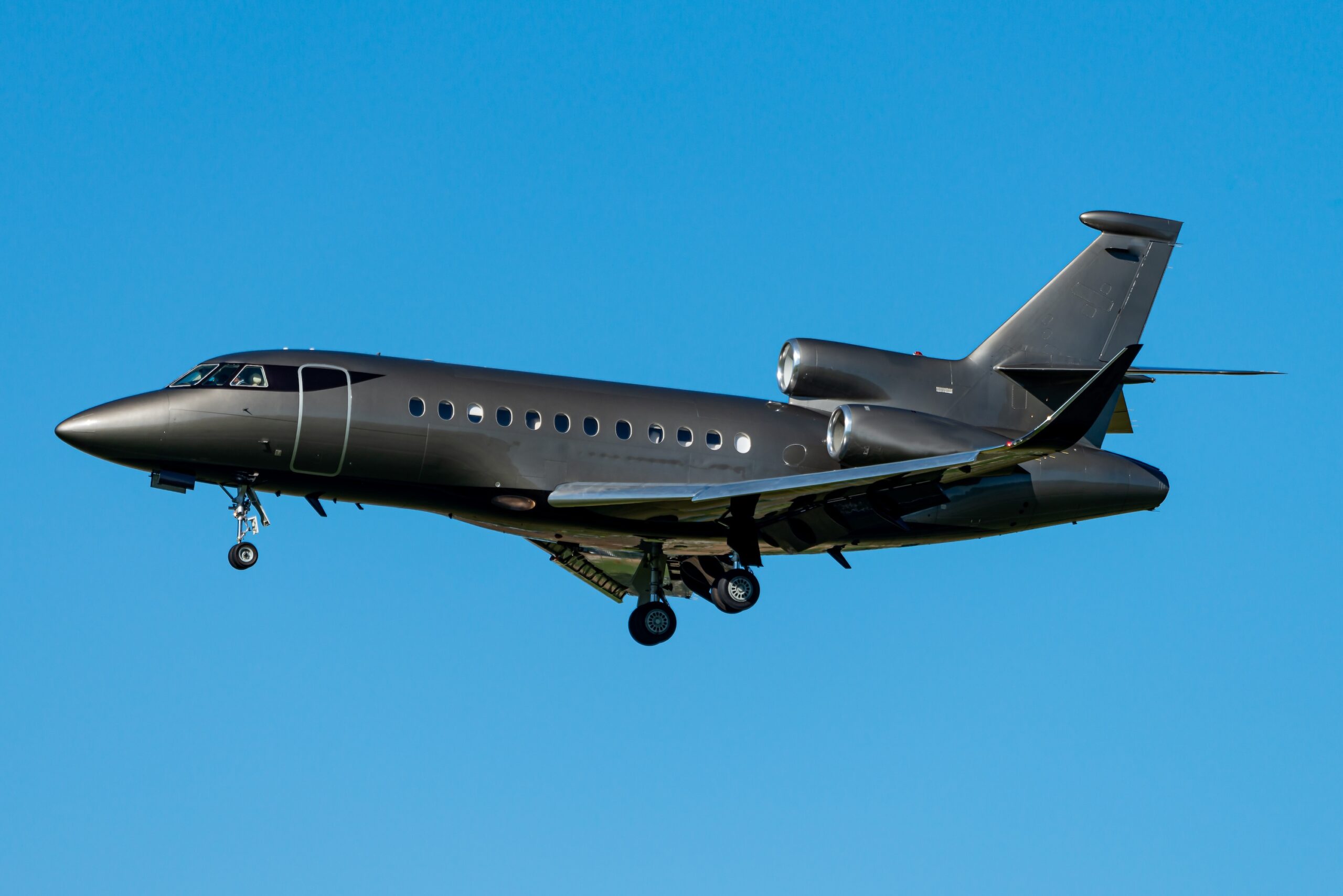 Dassault Falcon private jet on approach to land with blue sky background and all black paint