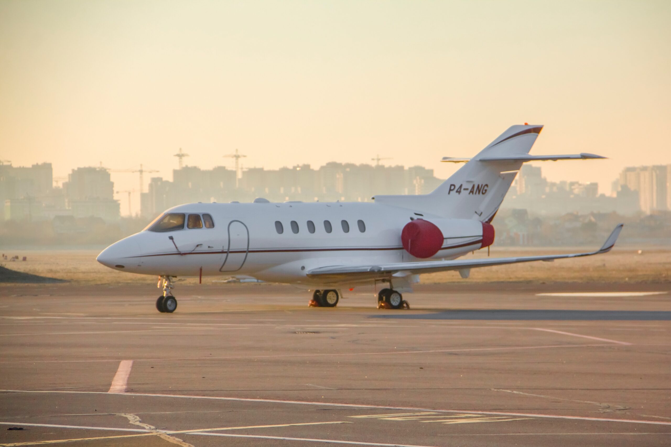 Hawker 900XP private jet reg number P4-ANG with engine covers on apron at airport at dawn