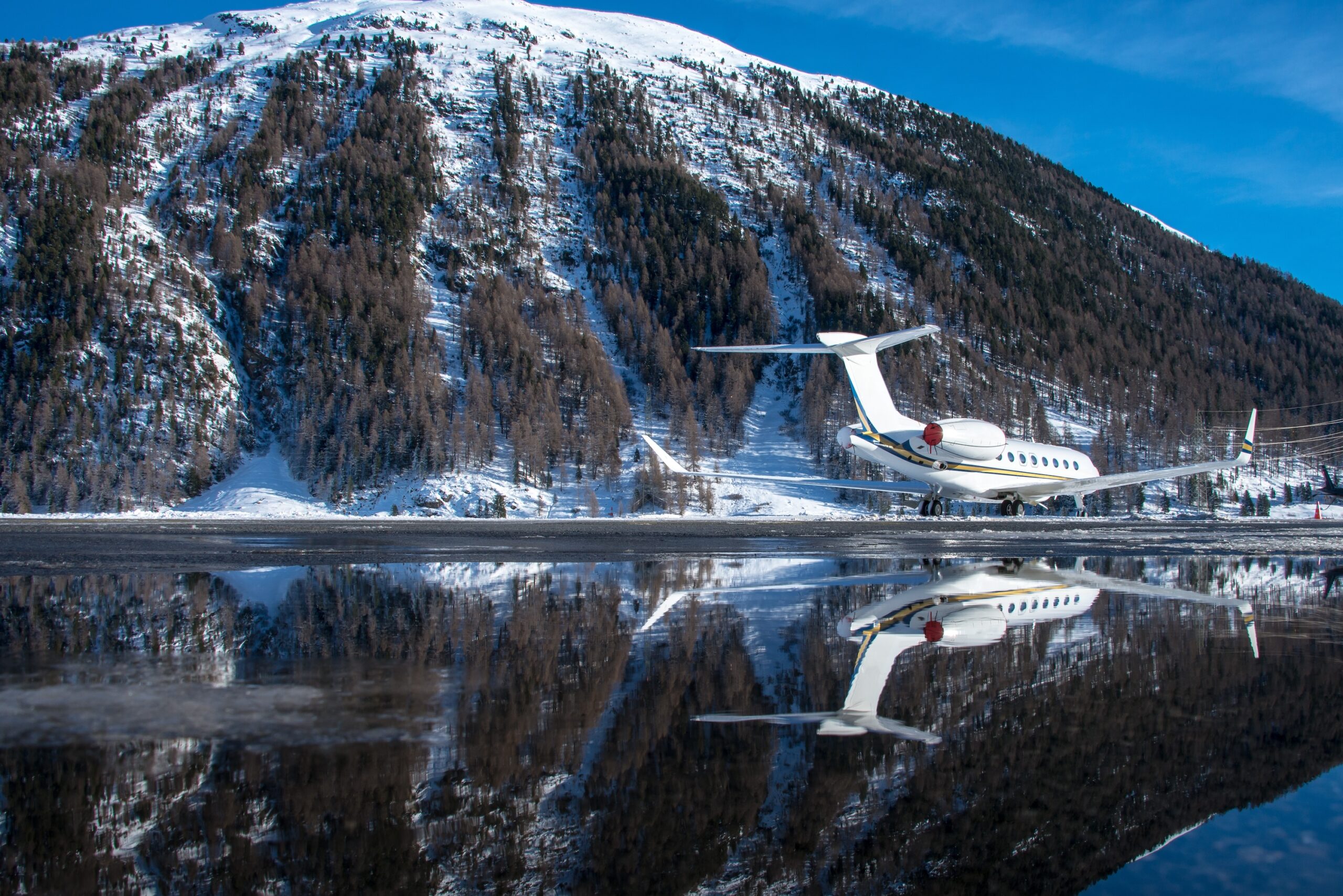 Rear view of private jet parked at airport with reflection in puddle of water at snowy mountainous Swiss airport