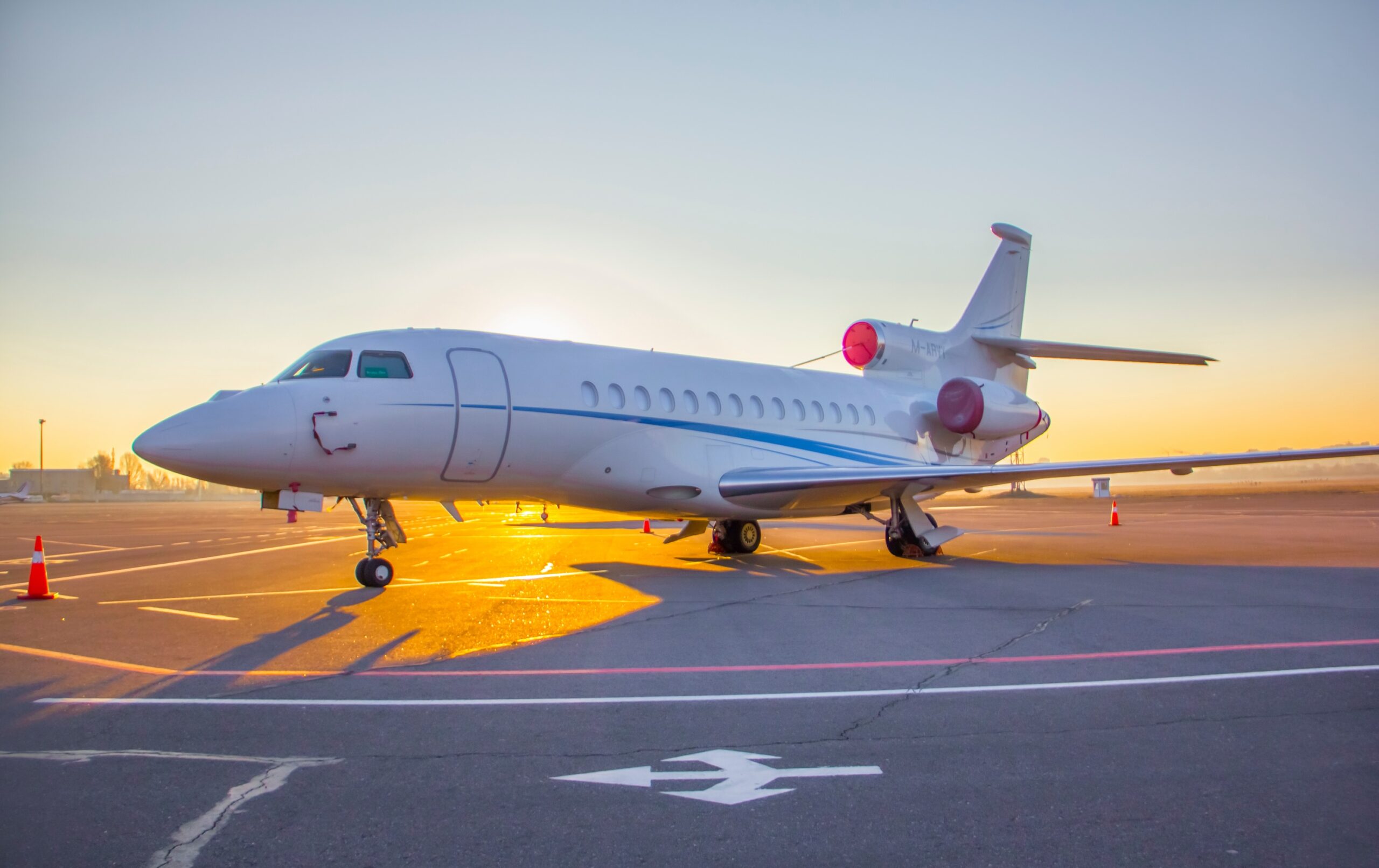 Dassault Falcon parked at airport with engine covers and sun rising behind