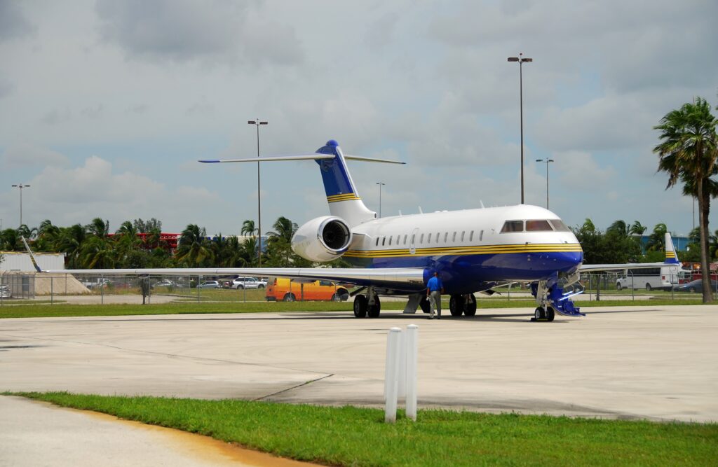 Bombardier Global 5000 private jet with blue, yellow and white paint on apron with stairs down and man next to it
