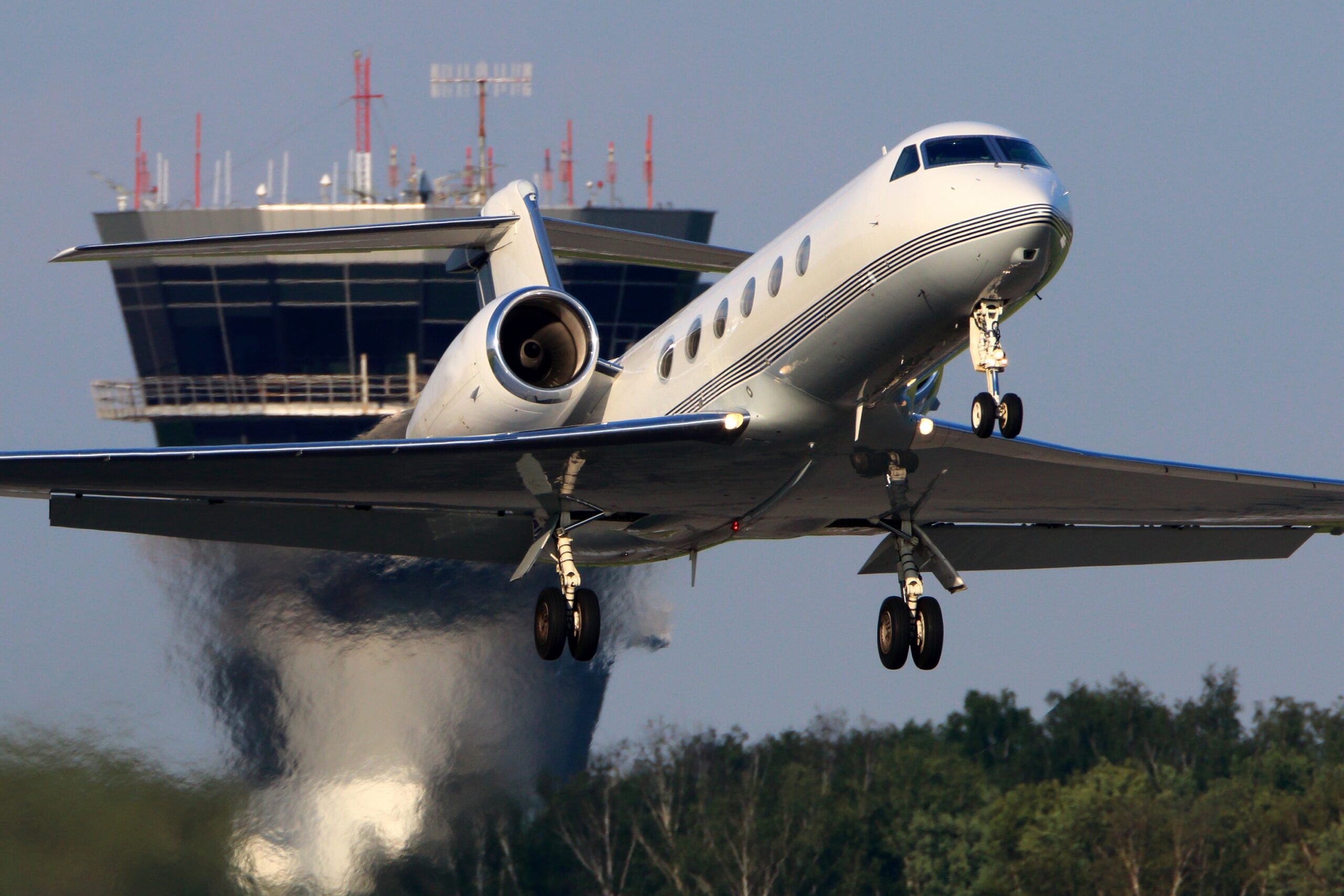 White Gulfstream with jet exhaust visible taking off from airport