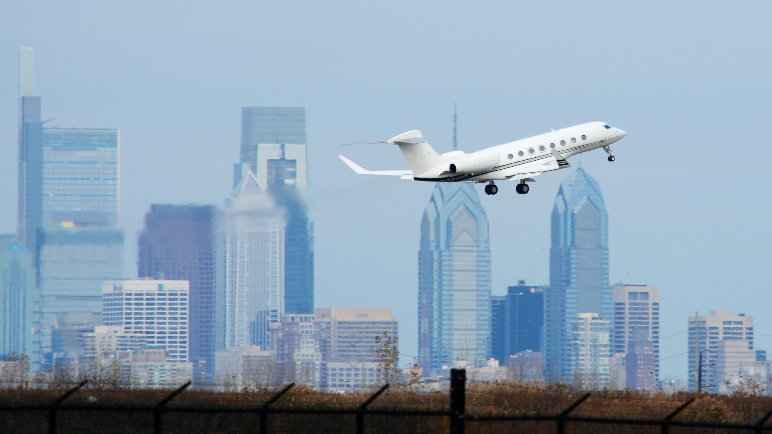 Gulfstream taking off with jet exhaust visible behind it and the Philadelphia Skyline in the distance