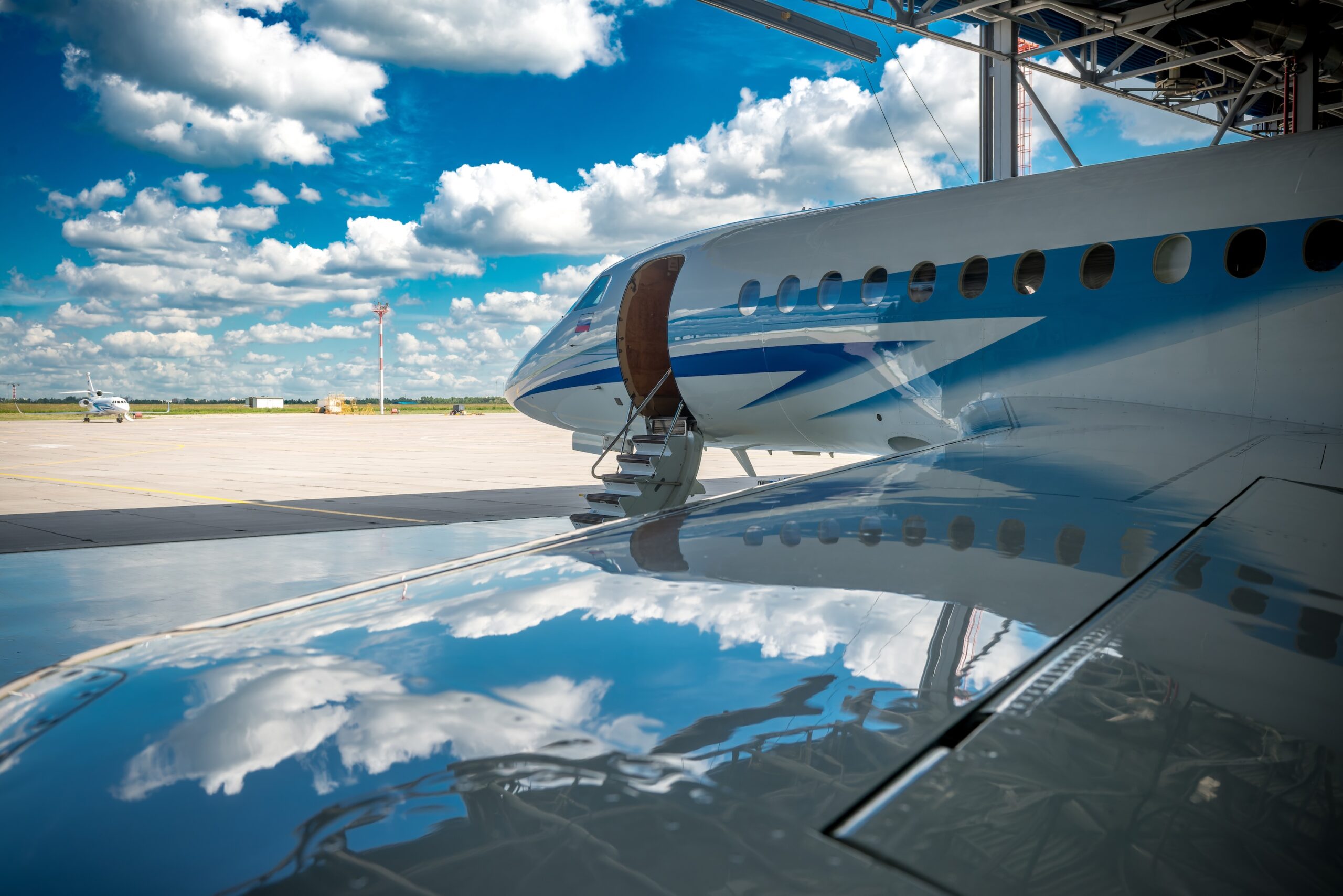 The blue sky with clouds is reflected on the wing of a private jet in a hangar