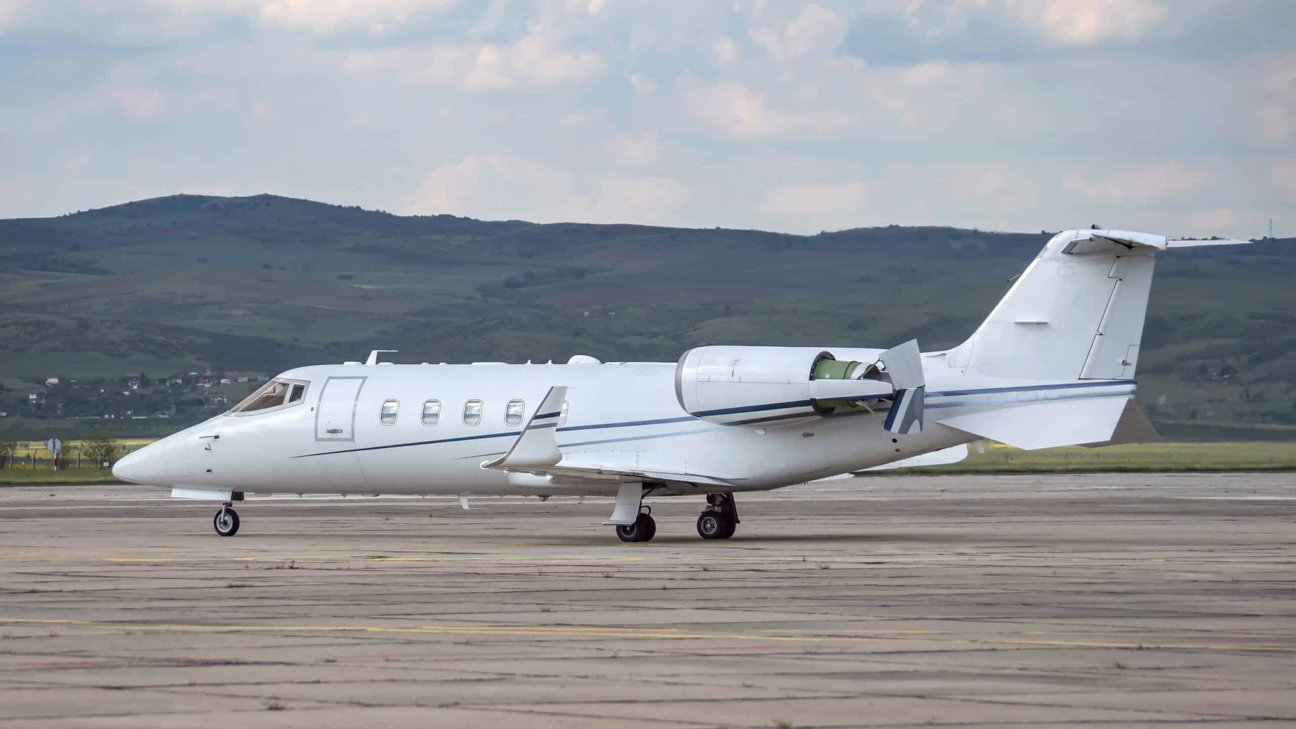 Side view of white Learjet on apron of airport with thrust reversers engaged