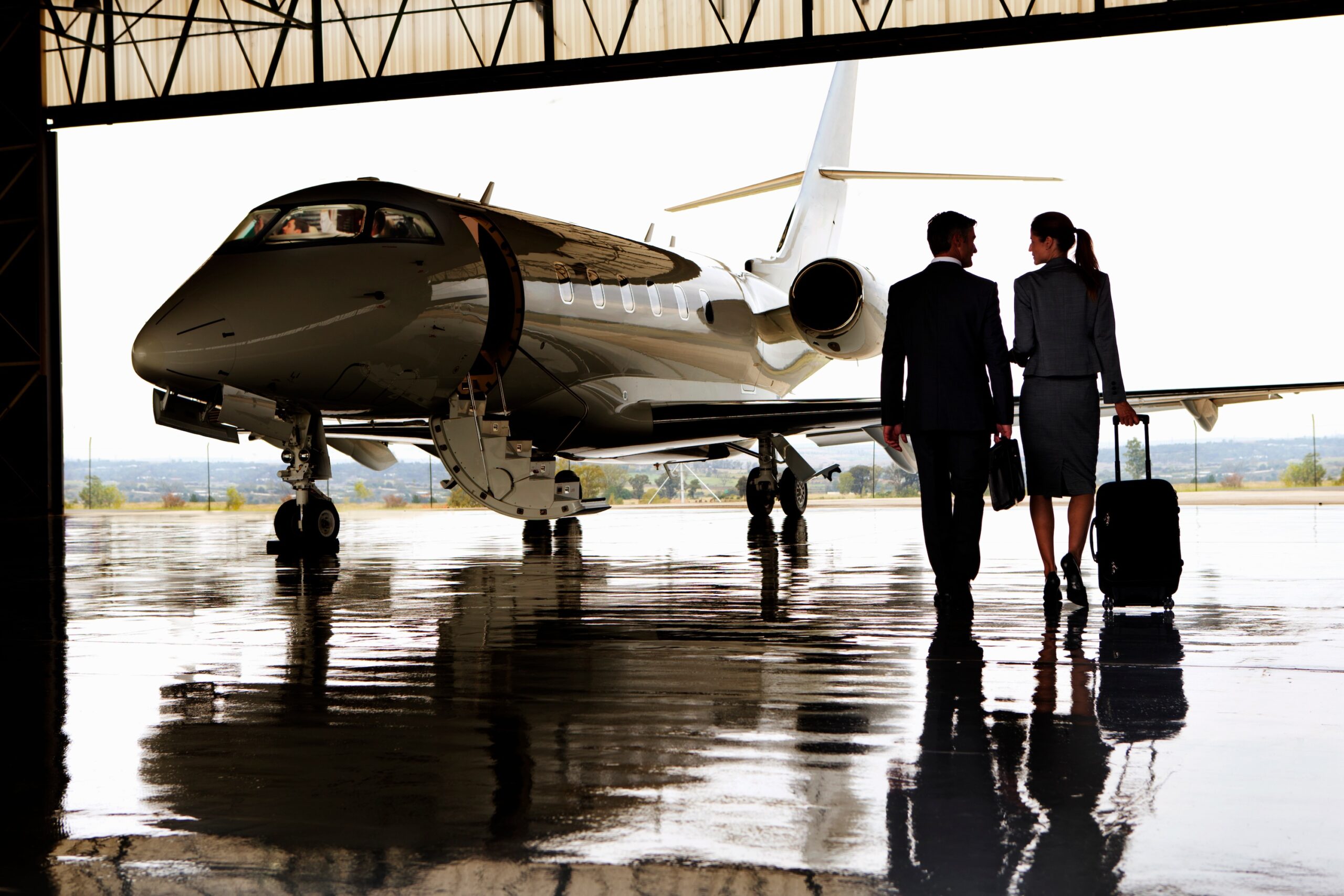 Wide shot of two business professionals walking towards private jet in hangar
