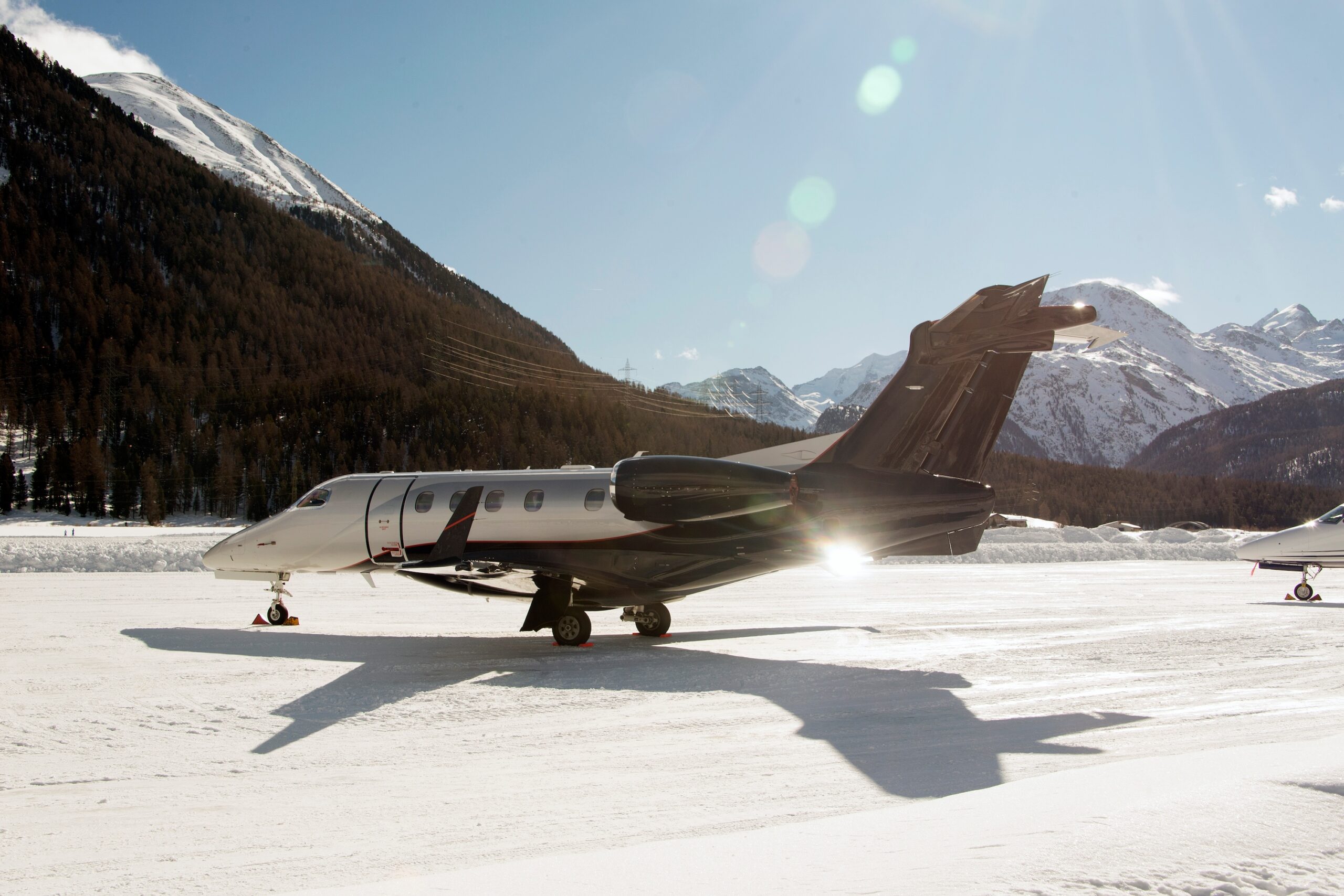 Embraer Phenom 300 light jet on the ground at snowy airport of Engadine St Moritz with mountains behind