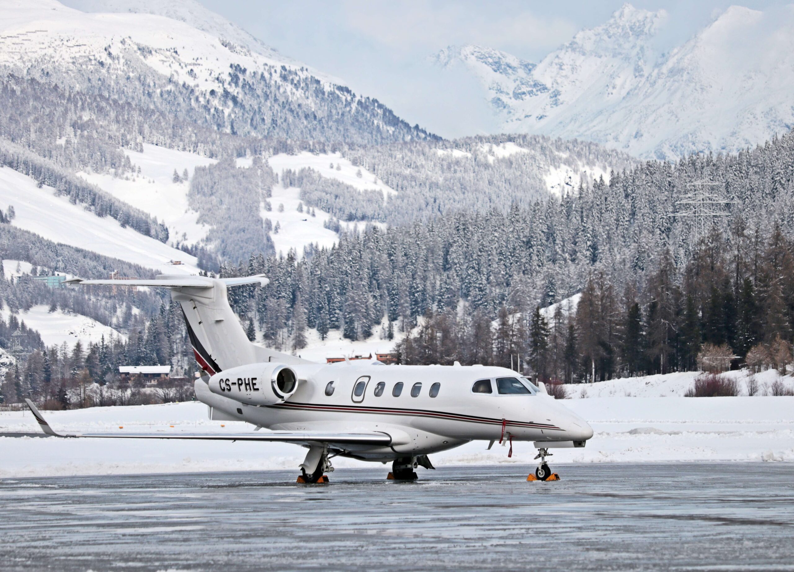 Embraer Phenom 300 reg number CS-PHE on ground at snowy airport with mountains in background