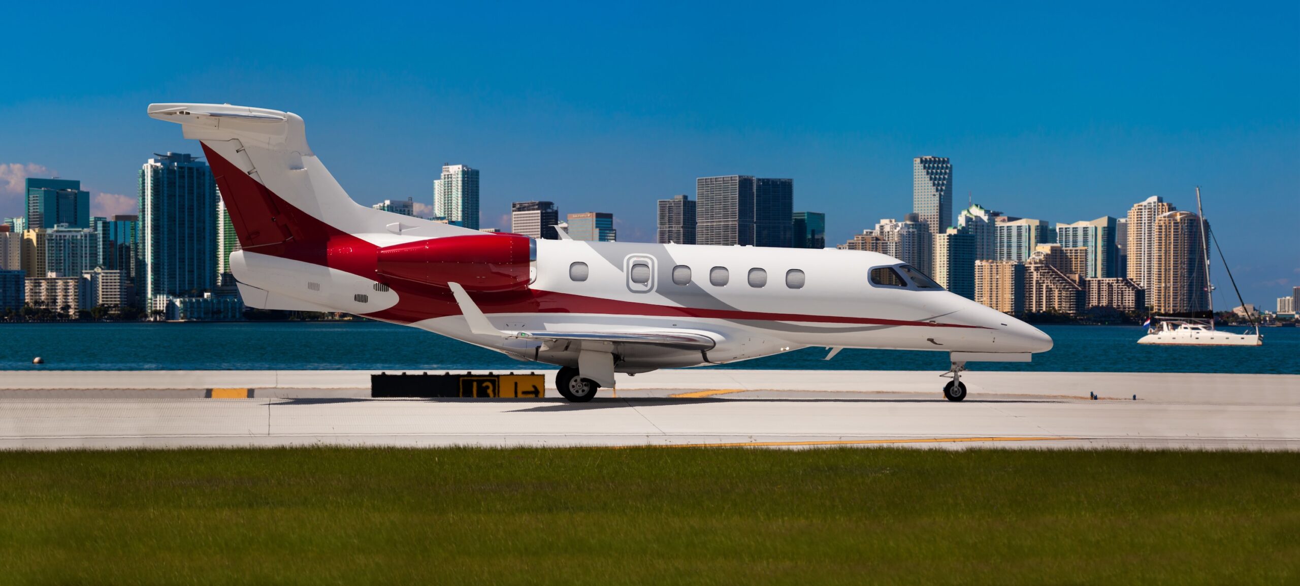 Embraer Phenom 300 private jet with red tail at airport with water and city skyline behind