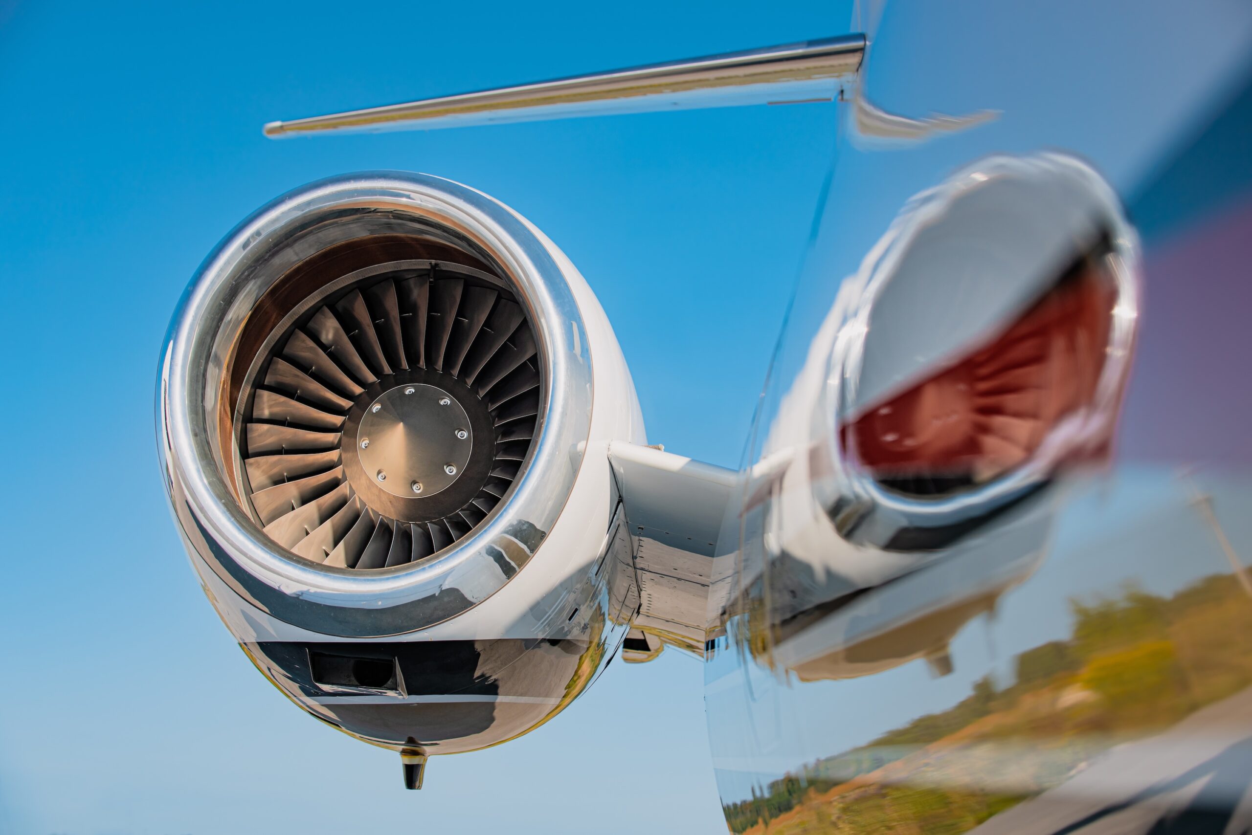 High mounted jet engine of a small business jet with a blue sky in the background. The jet engine is reflected in the fuselage