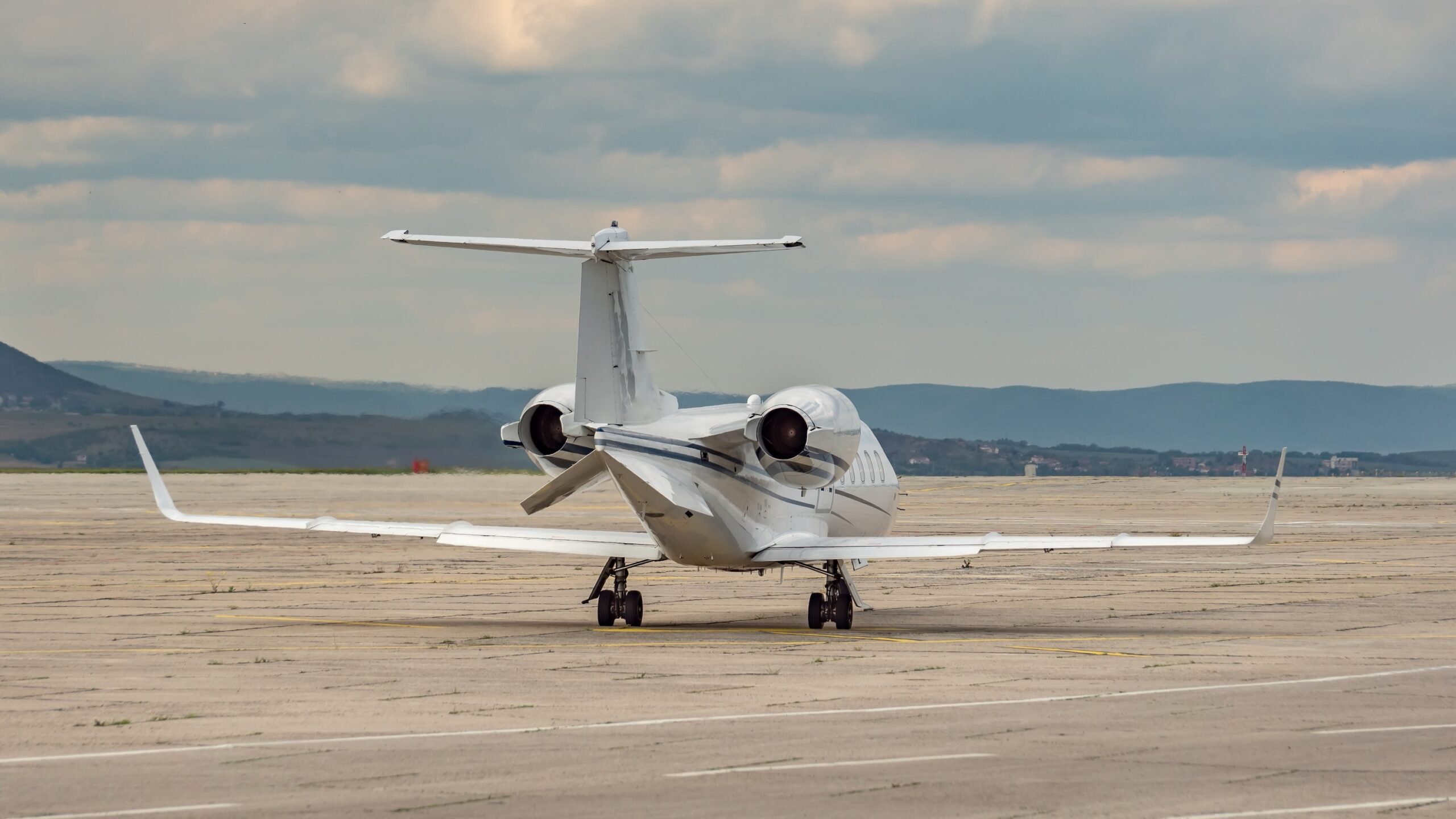 Back side view of small business jet. Dynamic cloudy sky over the airport.