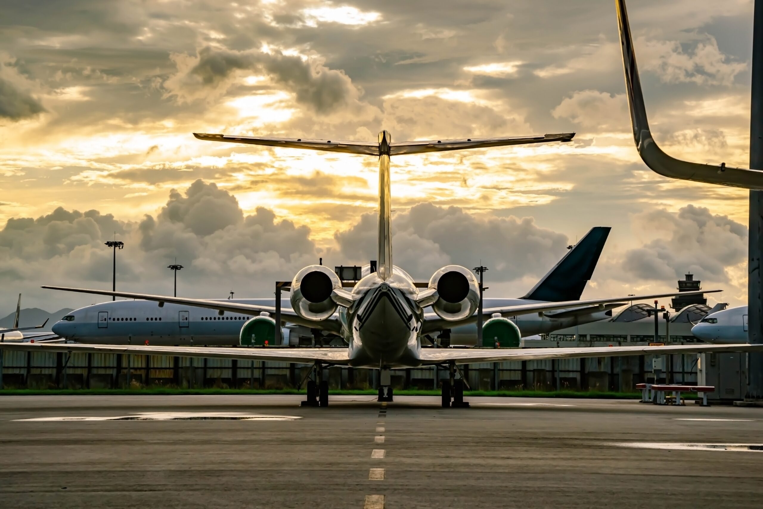 Rear view of private jet parked at airport with sun breaking through clouds behind