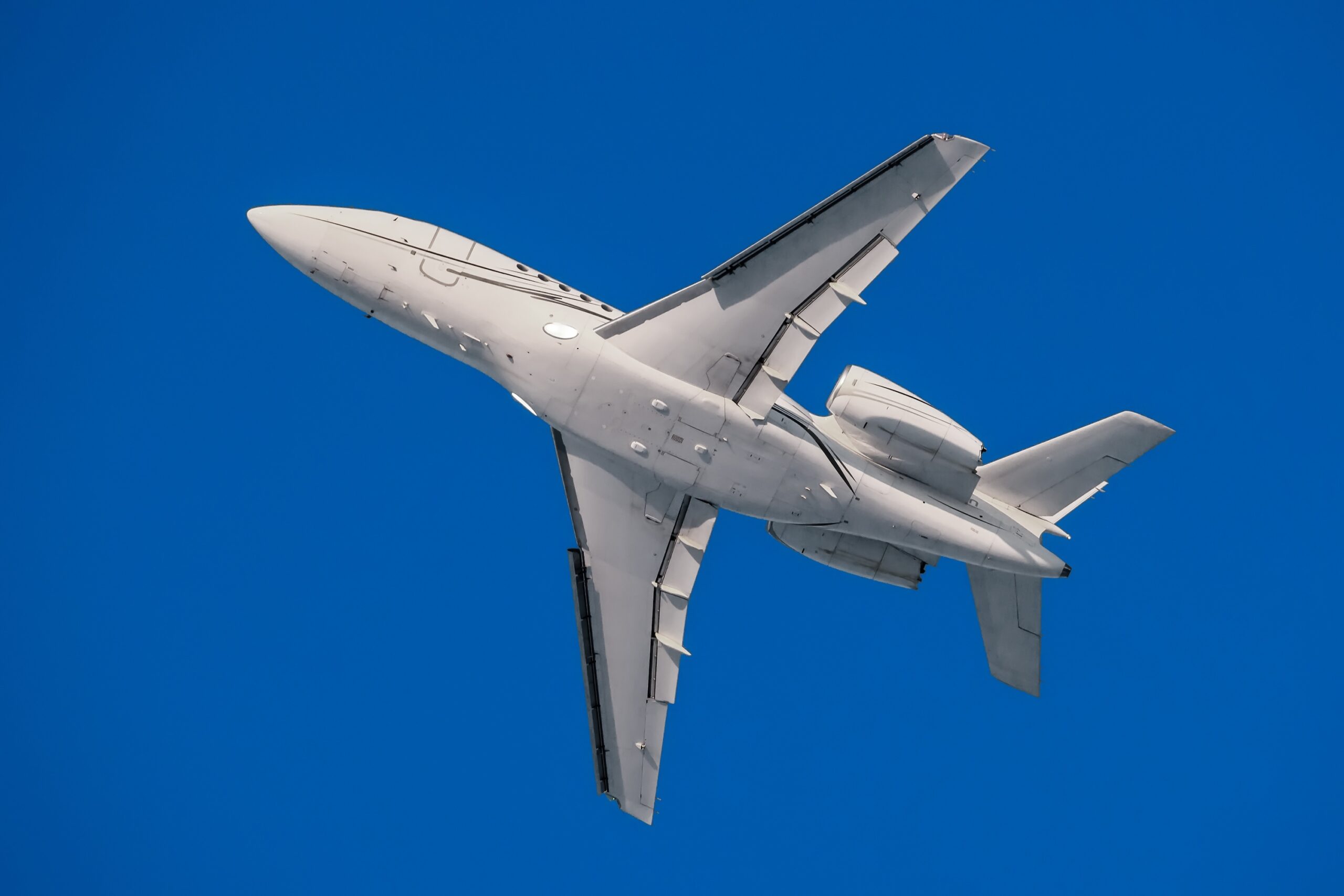 White modern private business jet in the flight underside view with blue sky