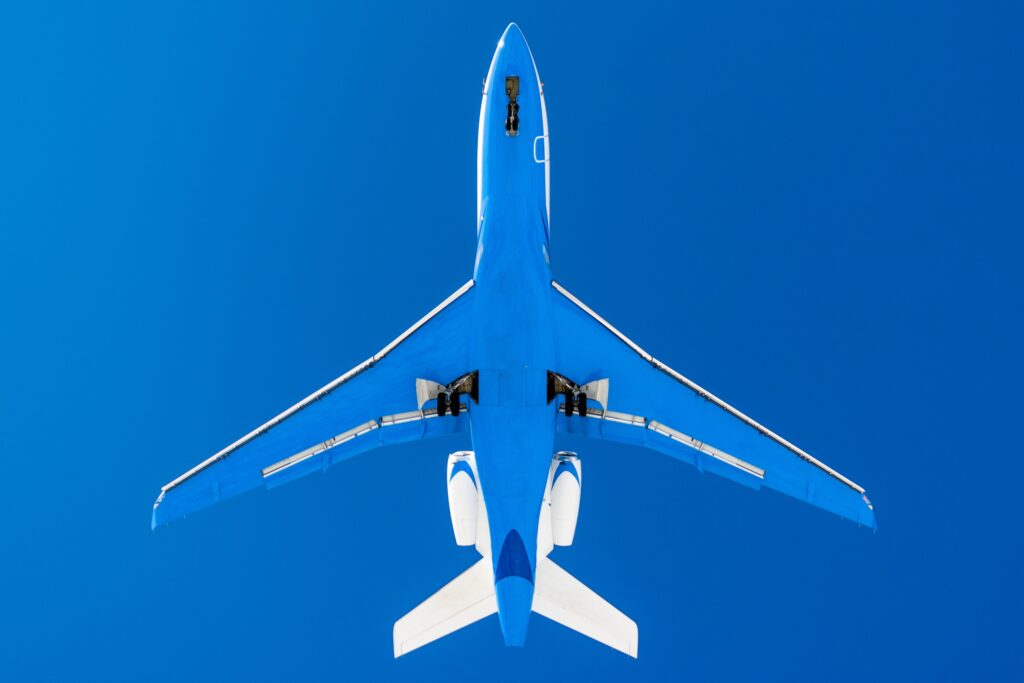 underside of private jet flying with blue bottom with blue sky, high in the sky