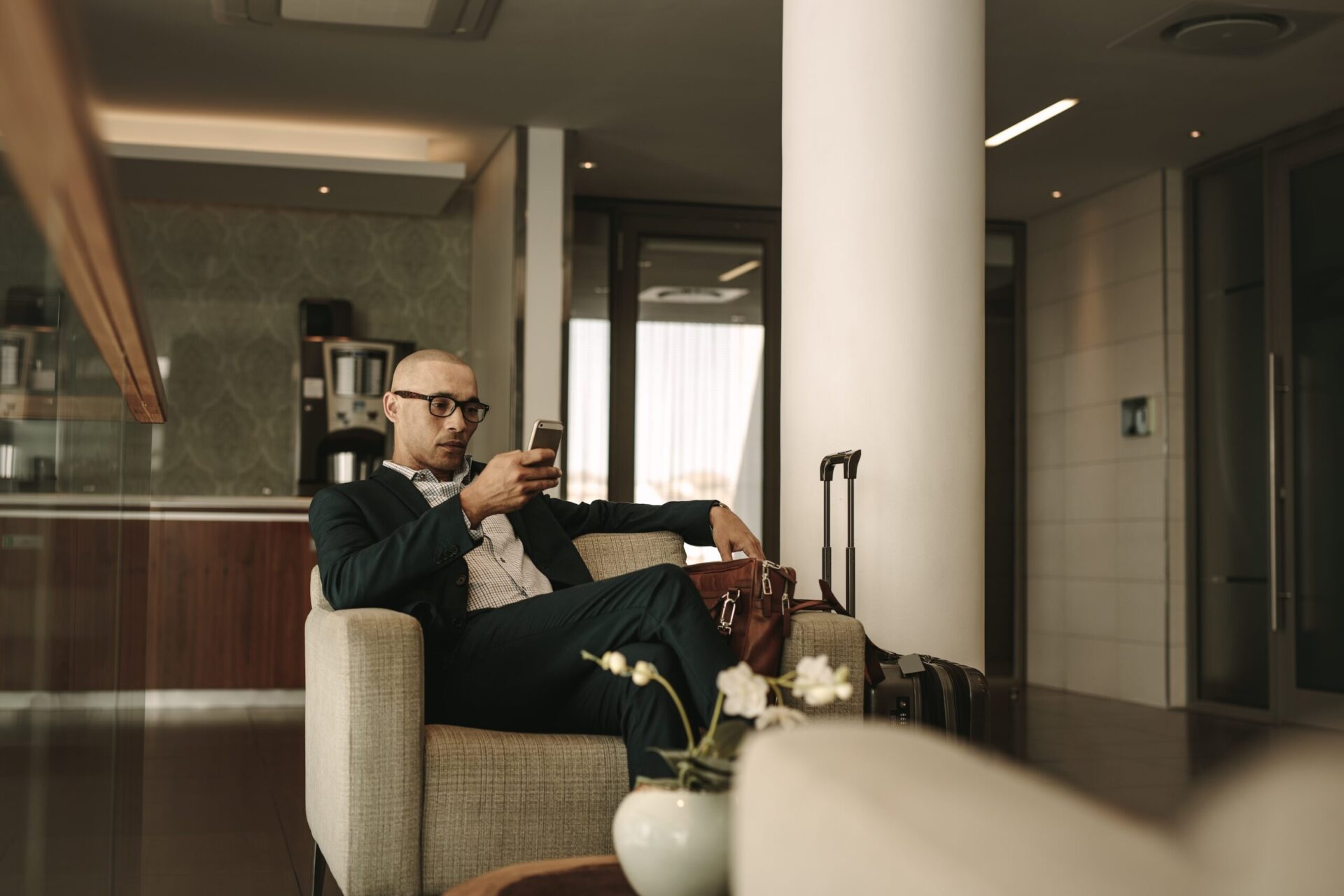 Business traveler waiting in airport lounge and using mobile phone. Businessman waiting for fight at airport lounge