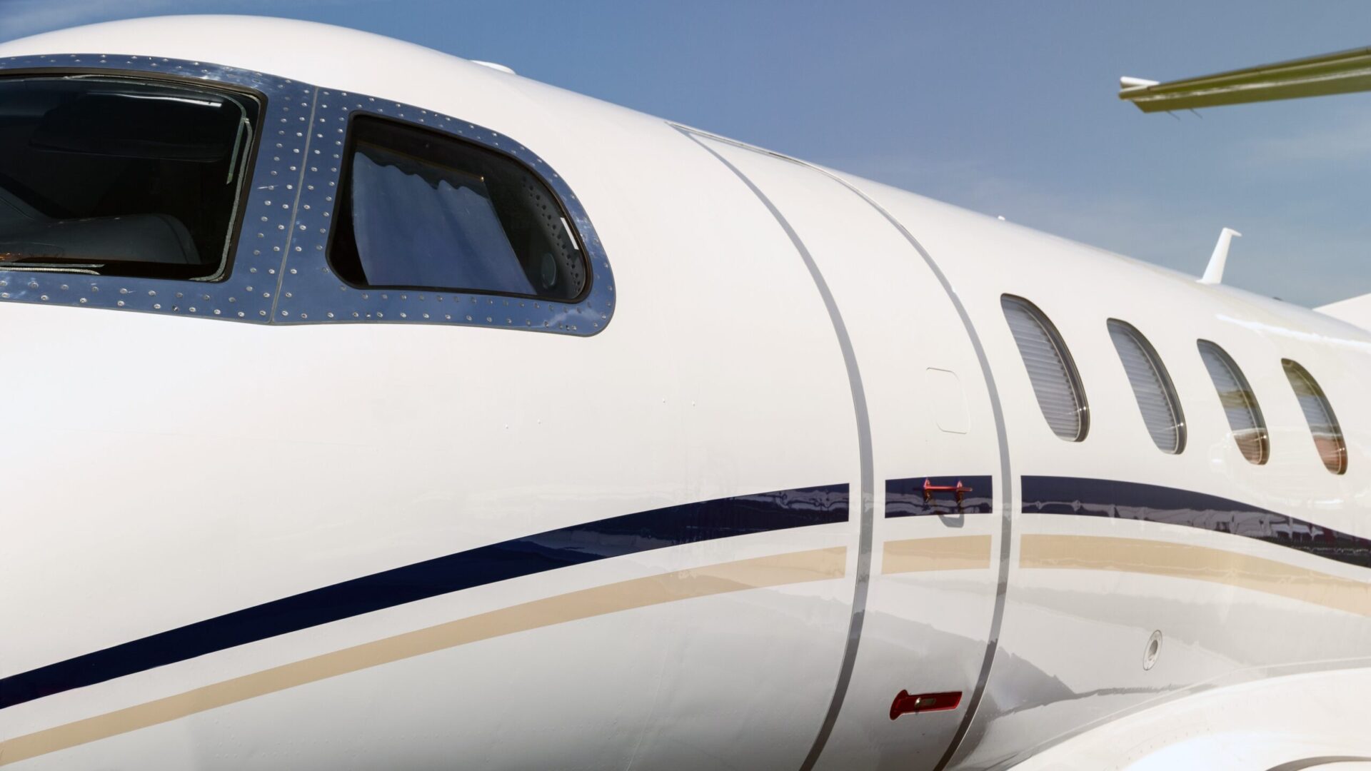 White modern business jet plane entrance door and cockpit windows close up.