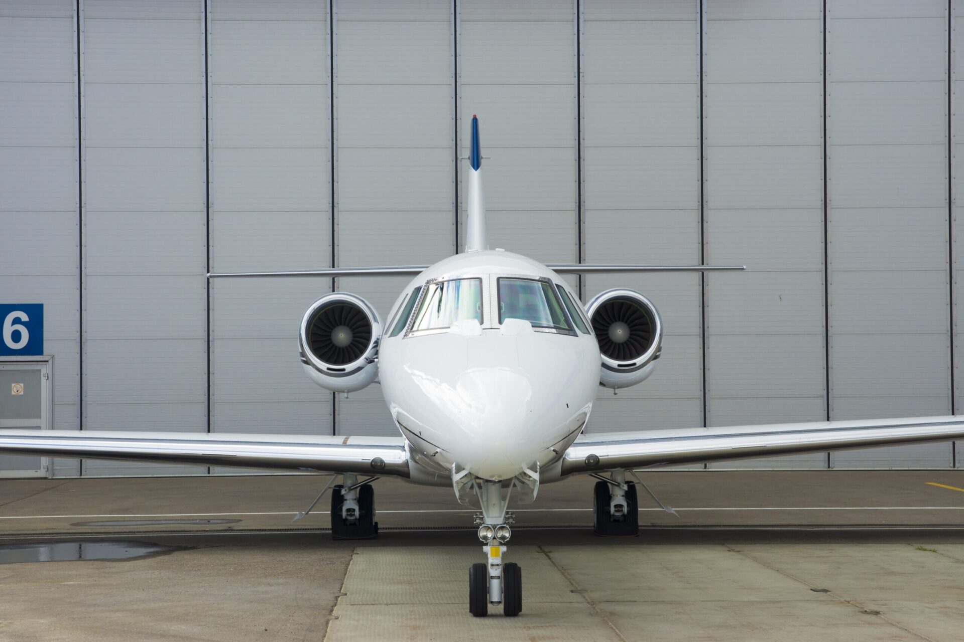 Nose on view of white jet in front of hangar
