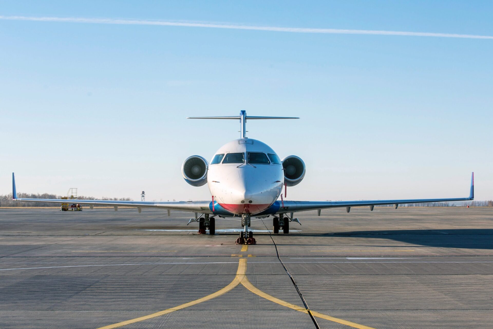 Full width nose on view of private jet parked at airport, white fuselage with red underside