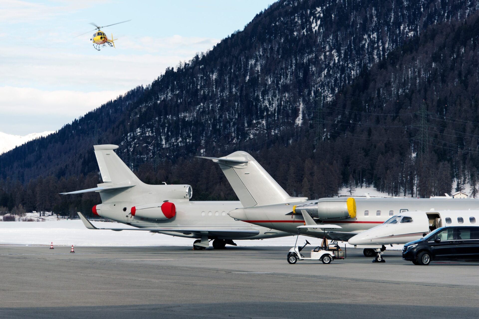 tail of large private jets at snowy airport with helicopter flying overhead