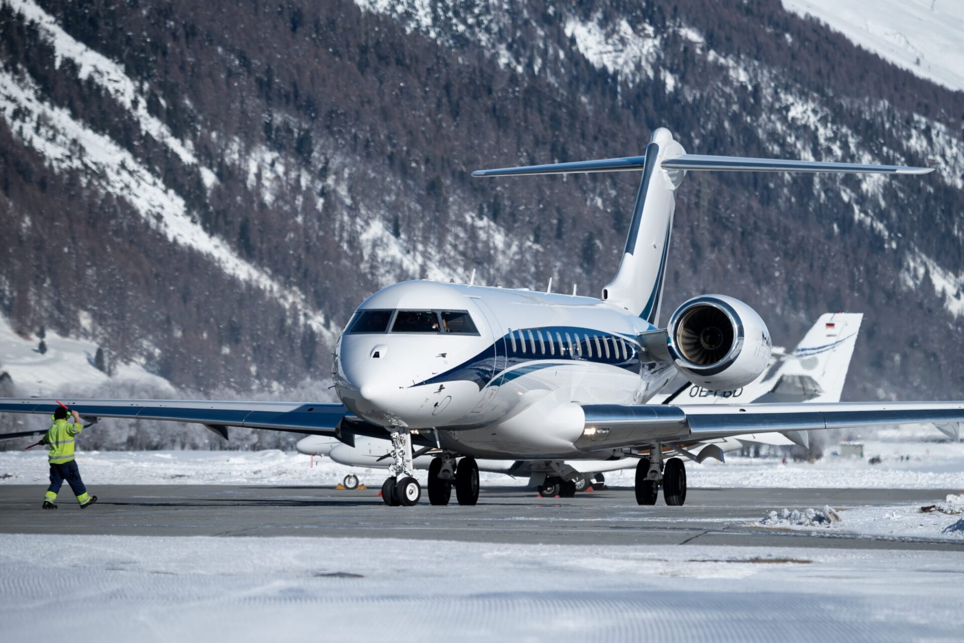 Bombardier Global 7500 taxiing at snowy airport with ground crew in front of it directing