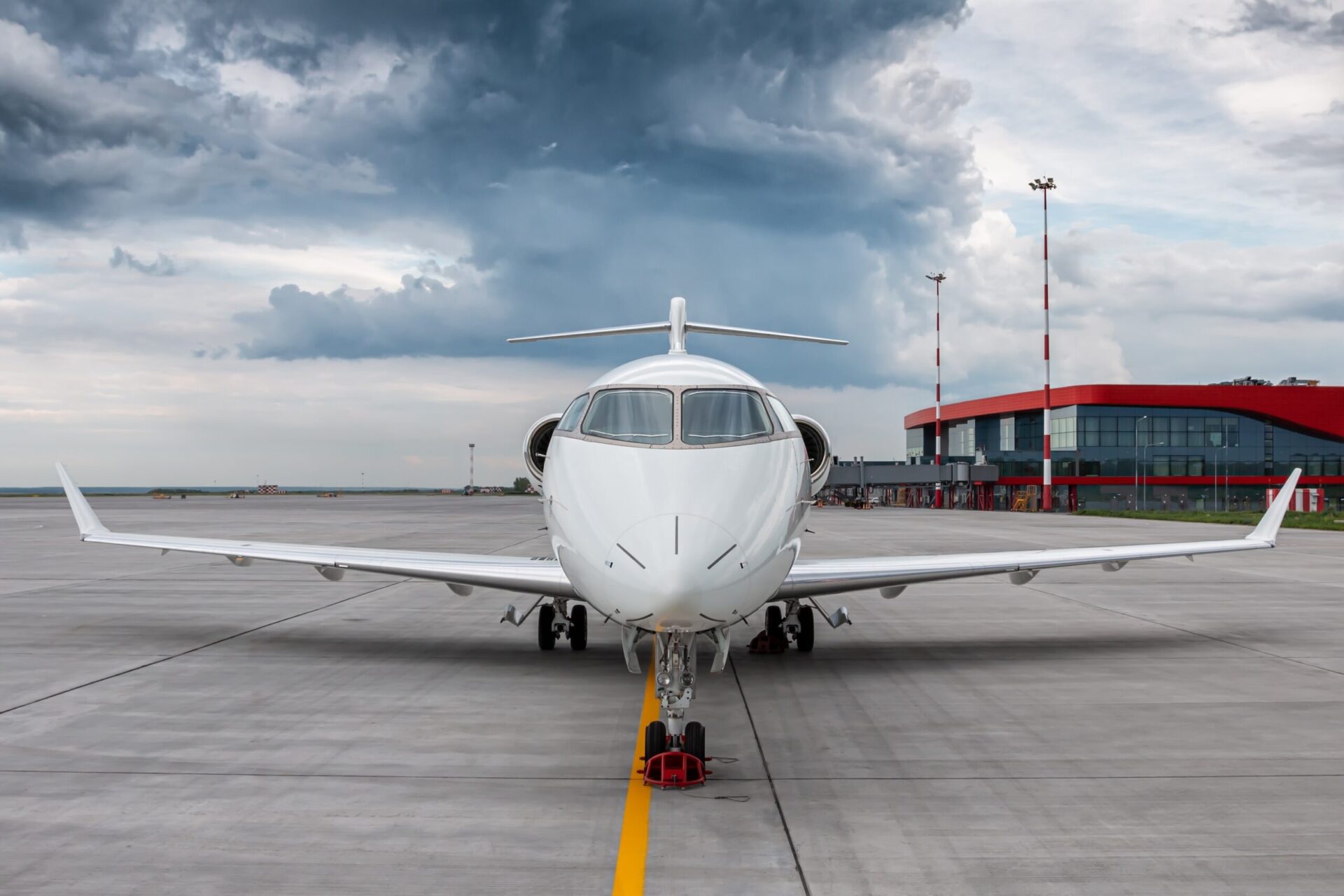 Nose view of white jet parked at airport with cloudy sky behind