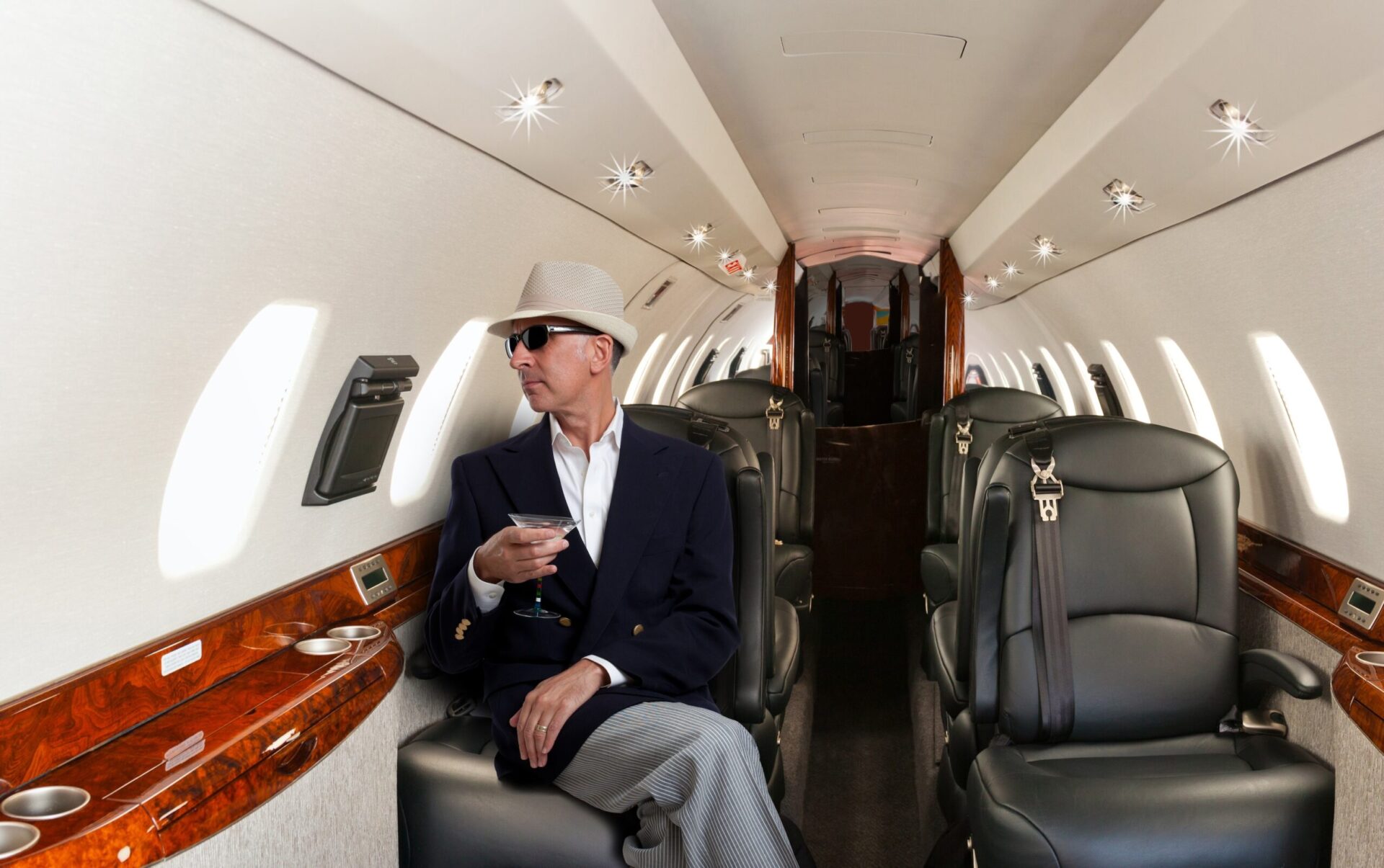 Confident mature man sitting at his seat in private airplane holding a cocktail