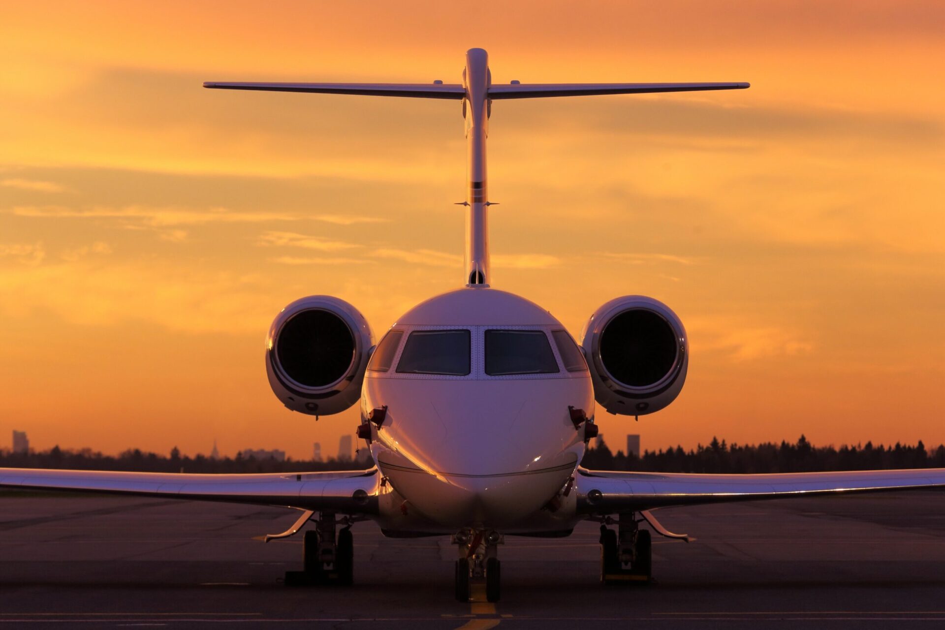 Front on view of business jet parked at airport with golden sky in the background