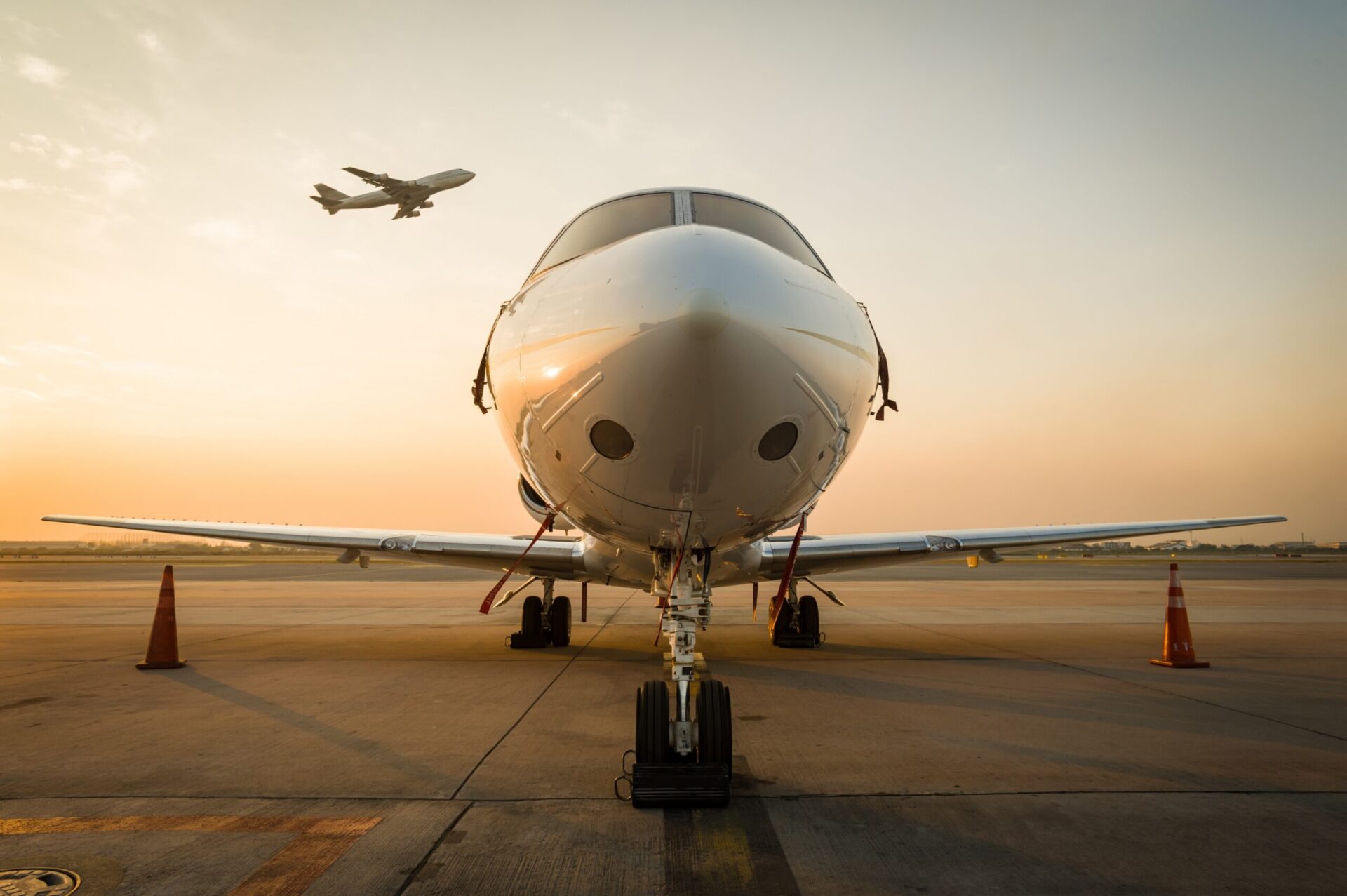 Nose view of private jet parked at airport at sunrise with 747 taking off in the background