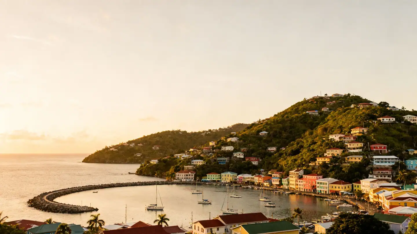 Grenada: a horseshoe harbor with colorful houses climbing green hills in golden-hour light
