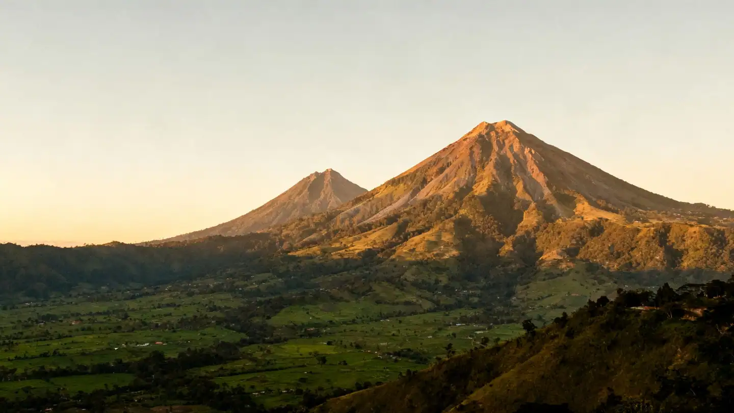 Guatemala's highlands: tall volcanoes above a green valley in golden-hour light