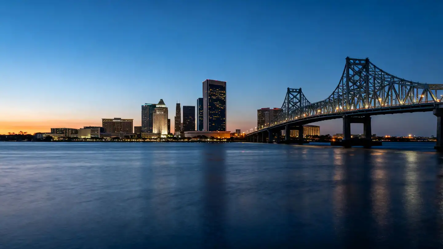 The Jacksonville skyline over the St. Johns River with a steel bridge at dusk