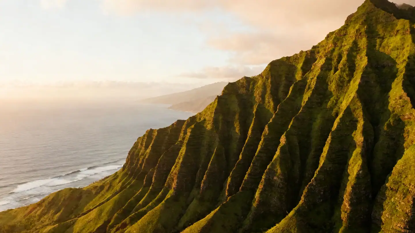 Kauai: the fluted green cliffs of the Na Pali coast above the ocean in golden-hour light