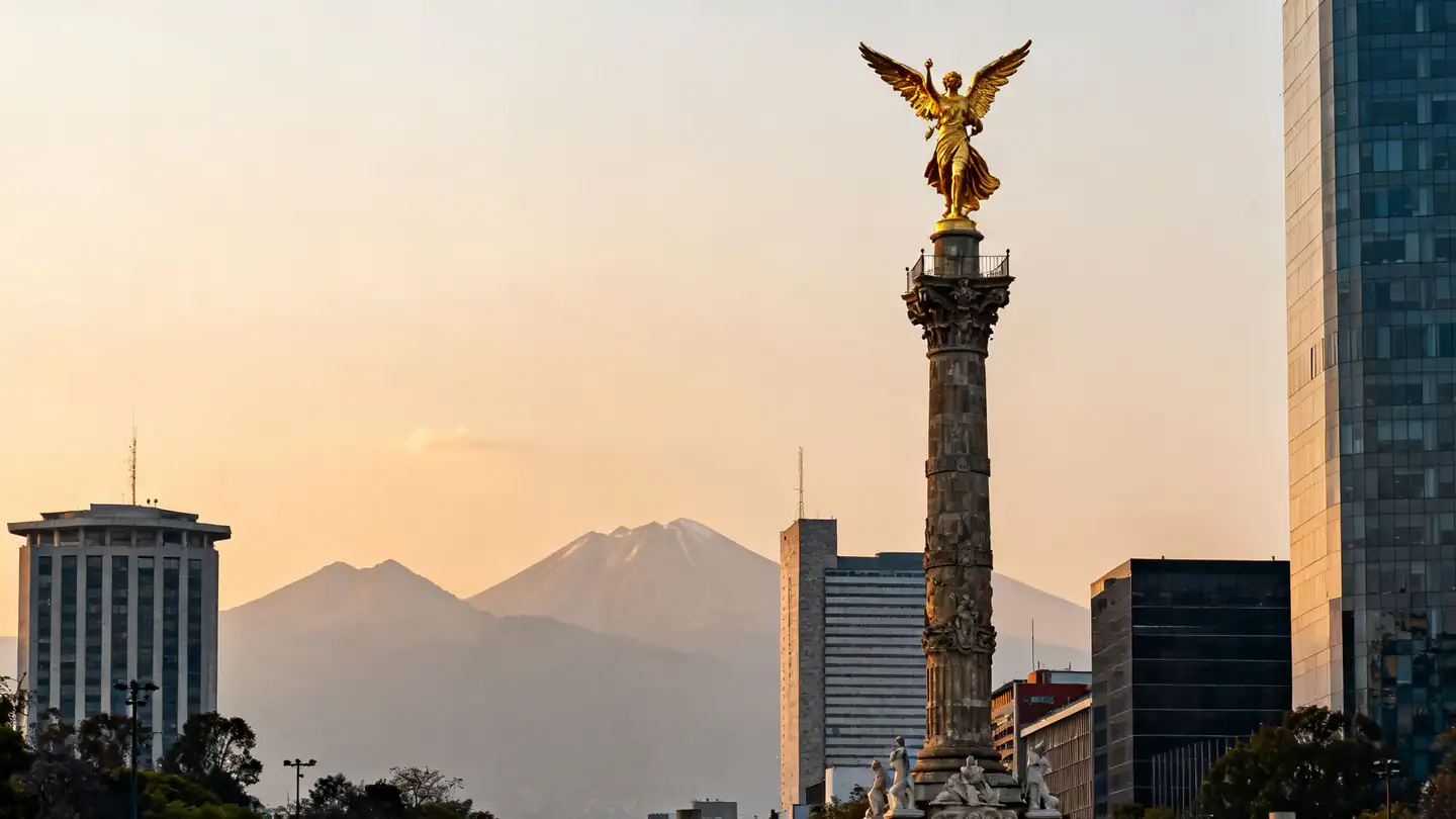 Mexico City's Paseo de la Reforma with a gilded angel column monument and modern towers at sunset