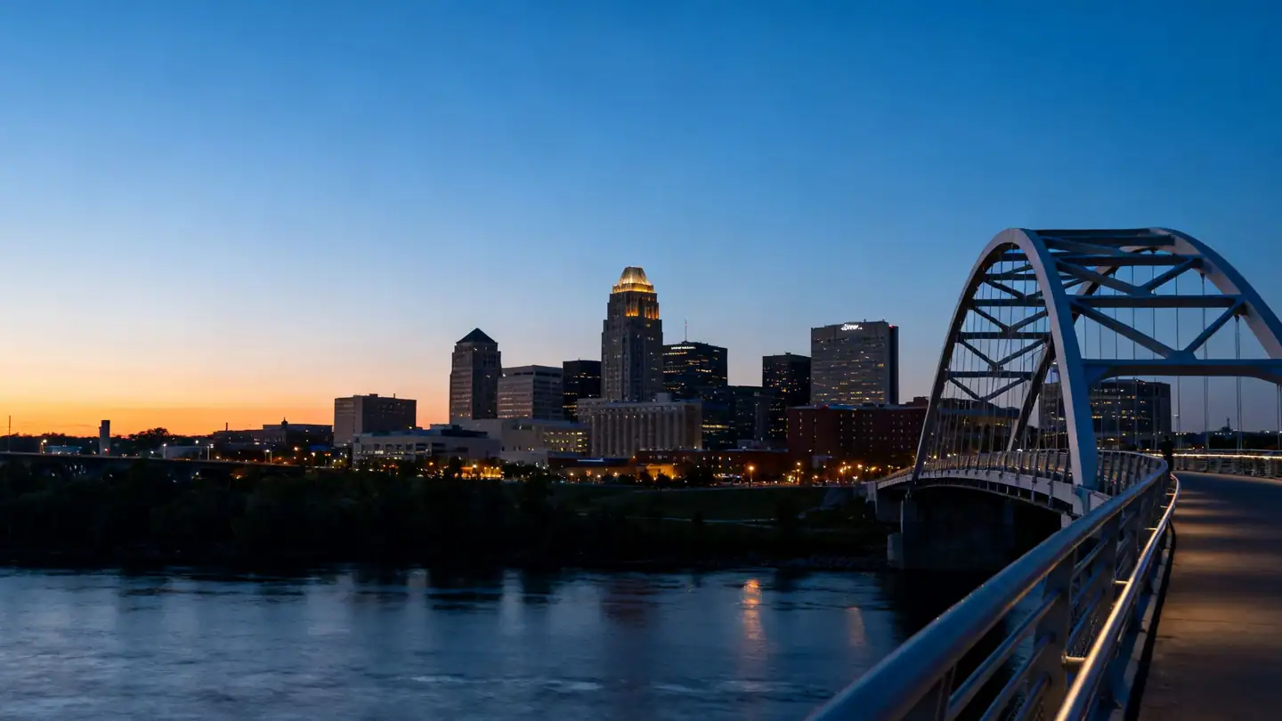 The Omaha skyline above the Missouri River with a curving pedestrian bridge at dusk