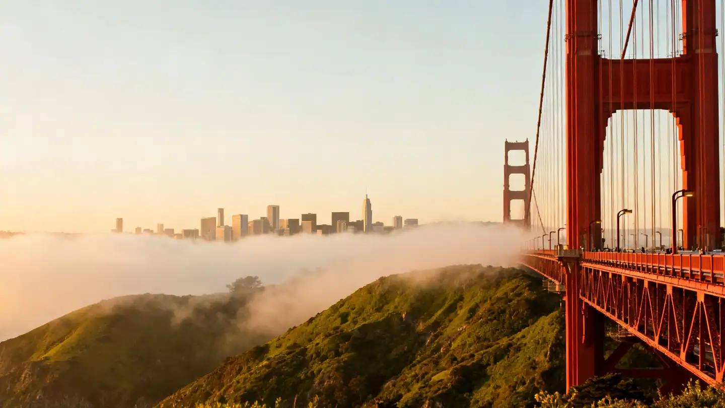 San Francisco Bay with a red suspension bridge at the edge of frame in golden-hour light