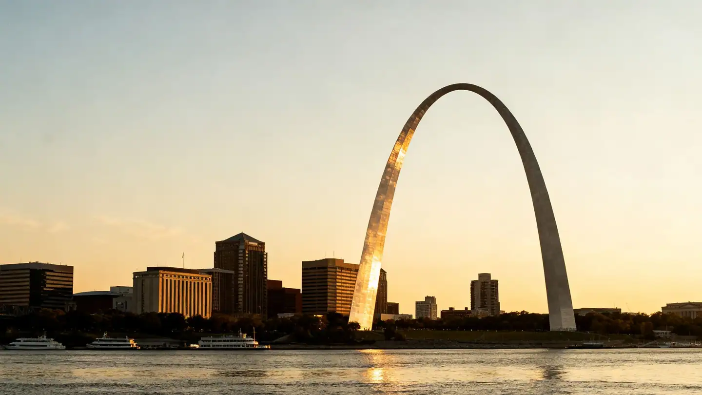 The St. Louis riverfront with a tall stainless-steel arch above the Mississippi River at sunset