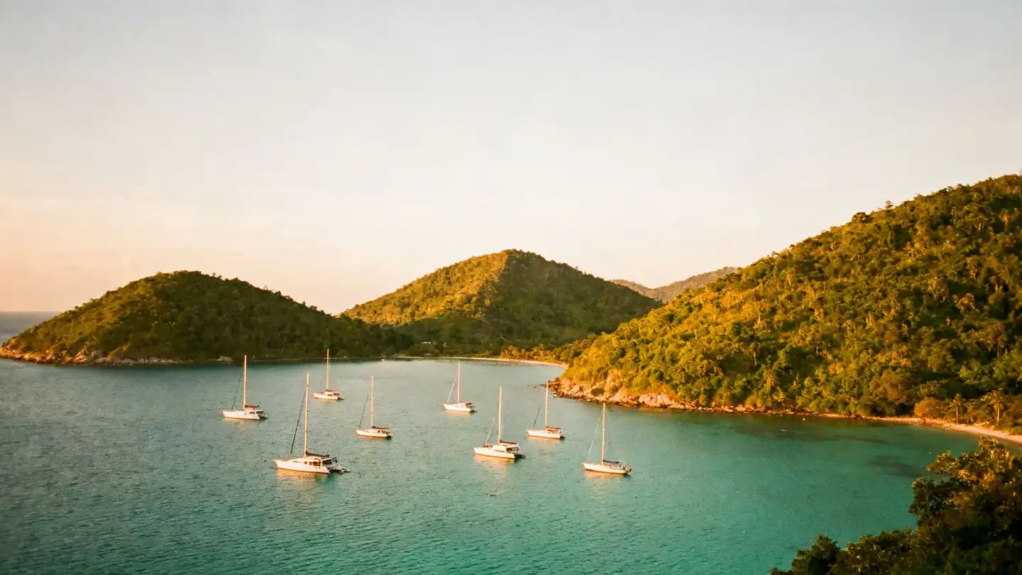 The British Virgin Islands: green hilly islands and sailboats anchored in a turquoise bay in golden-hour light